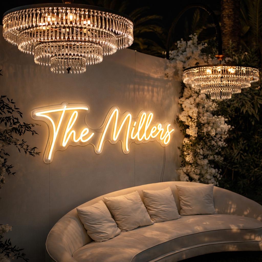a modern and elegant living space with a curved white sofa, a large chandelier, and a neon sign that reads "The Millers".