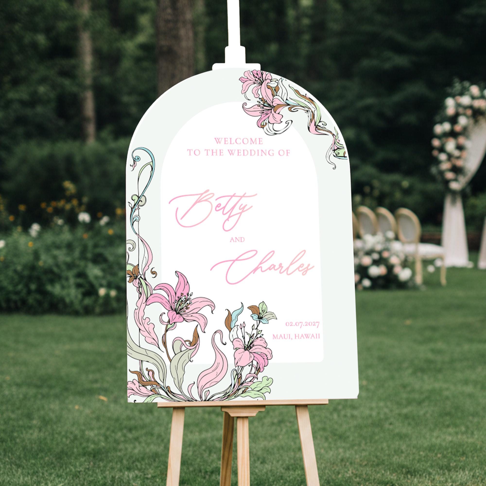 a white sign with floral designs and text, standing on a wooden stand in a grassy area.