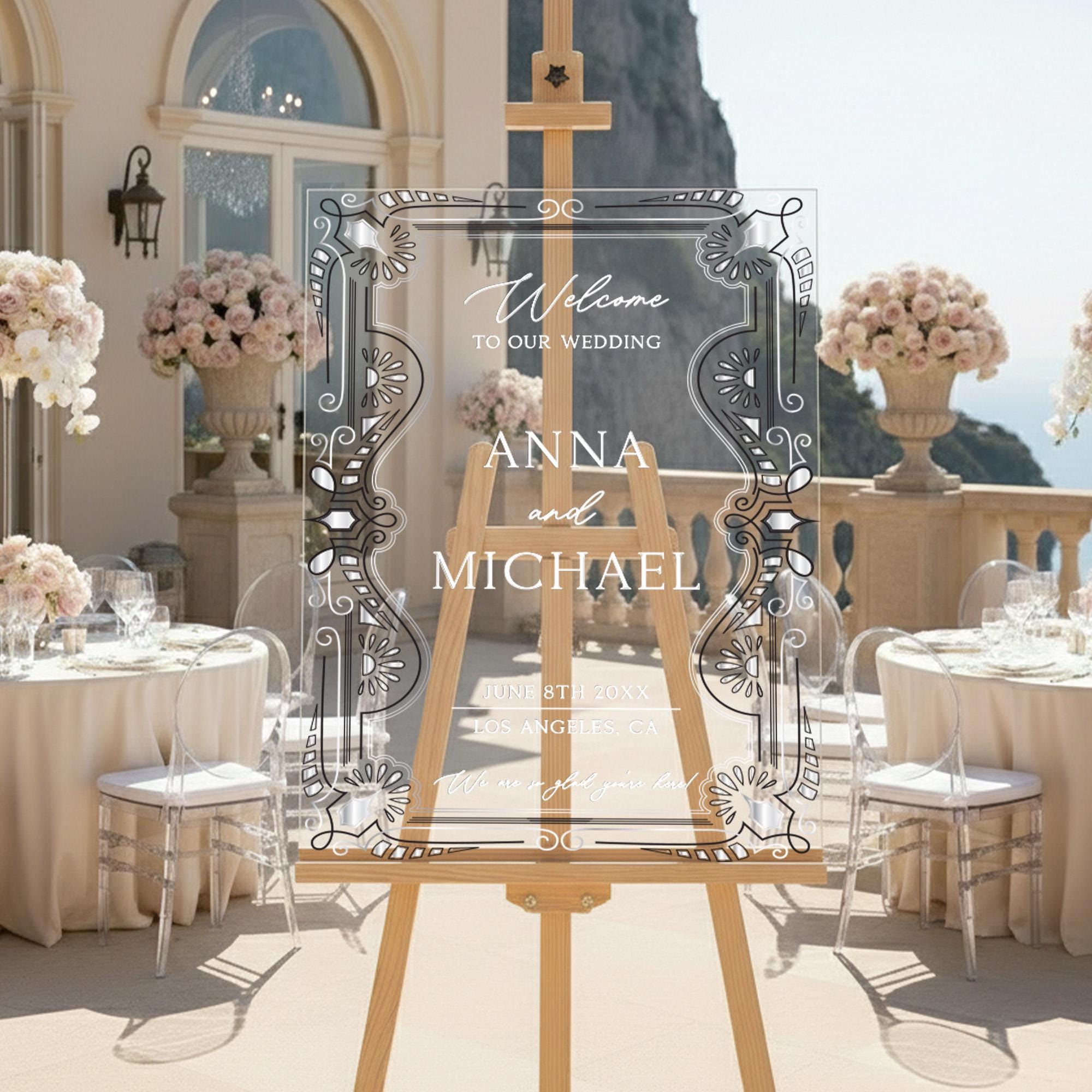 a wedding reception setup with a large wooden easel displaying a welcome sign for the newlyweds, Anna and Michael. The sign is surrounded by elegant floral arrangements and set up for a formal event.