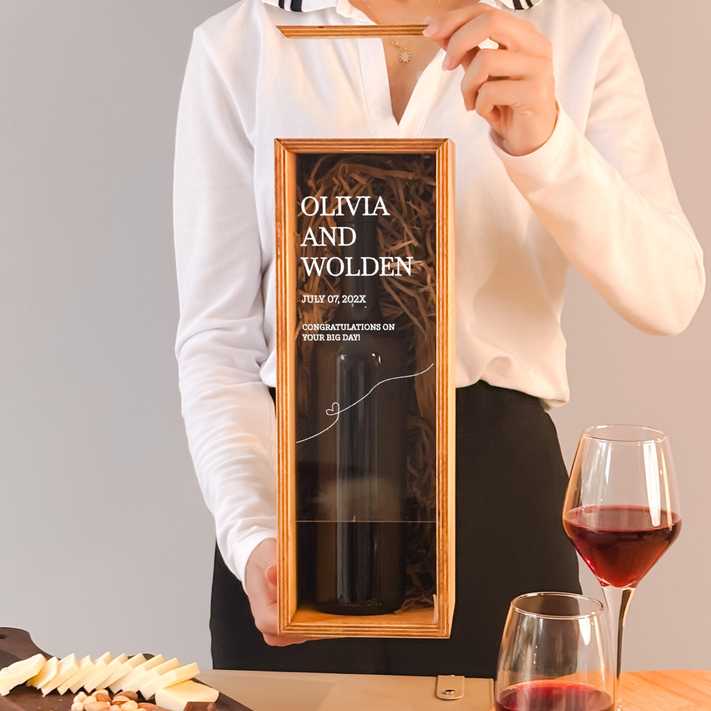 A person is holding a framed picture of a wine bottle, with a glass of red wine and cheese in front of them.