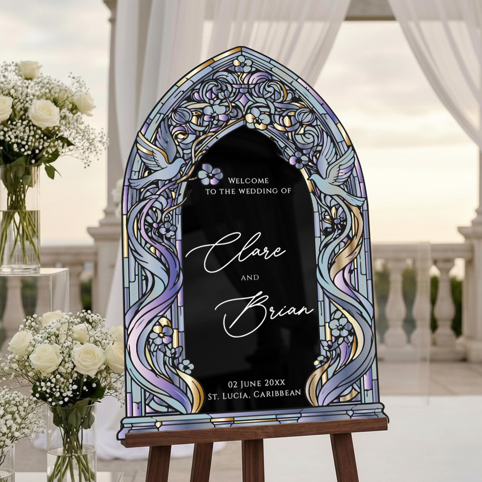 a wedding invitation sign with a stained glass design, placed on a wooden stand in front of a wedding venue.