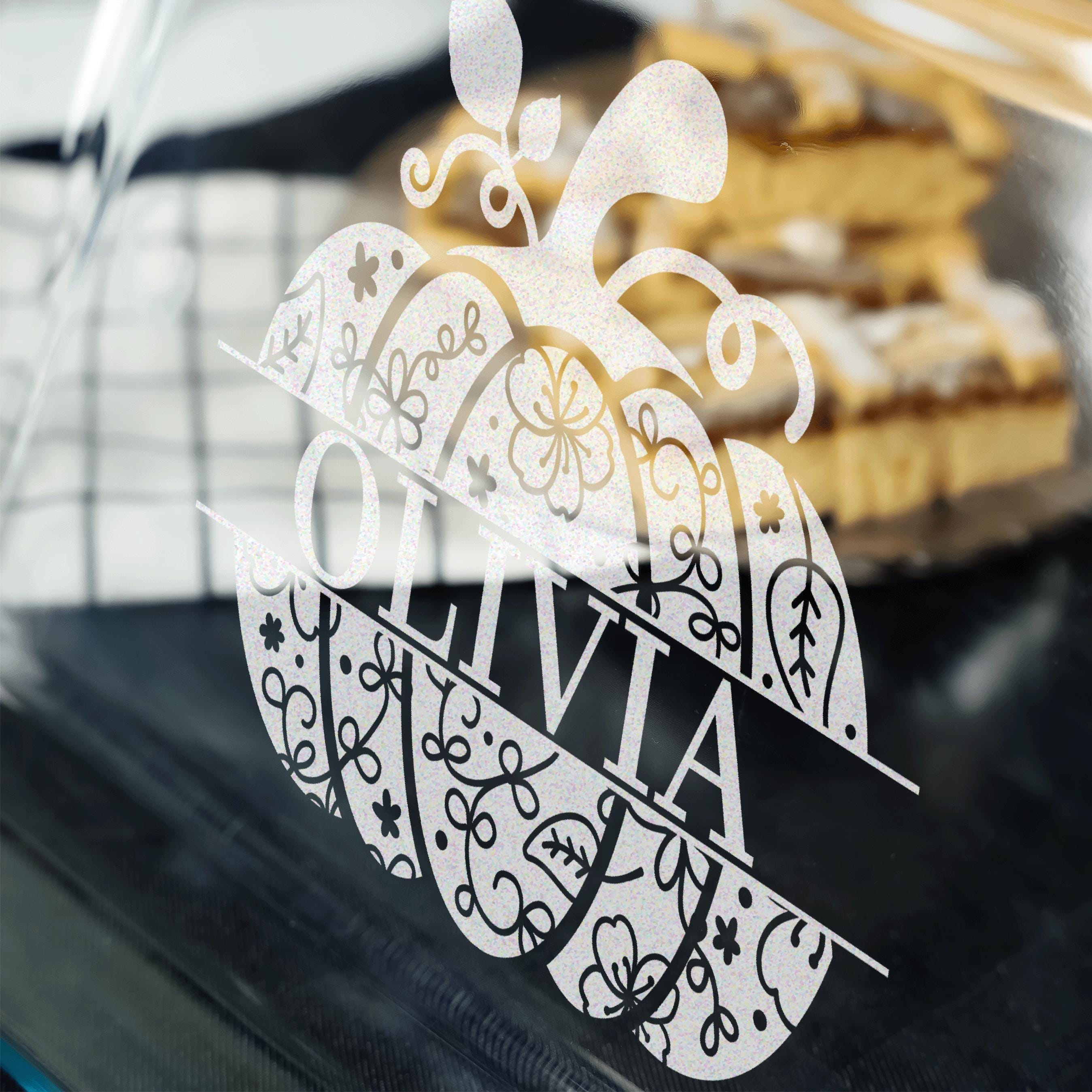 A close-up view of a glass surface with a decorative pumpkin-shaped design featuring the name "Olivia" written on it.