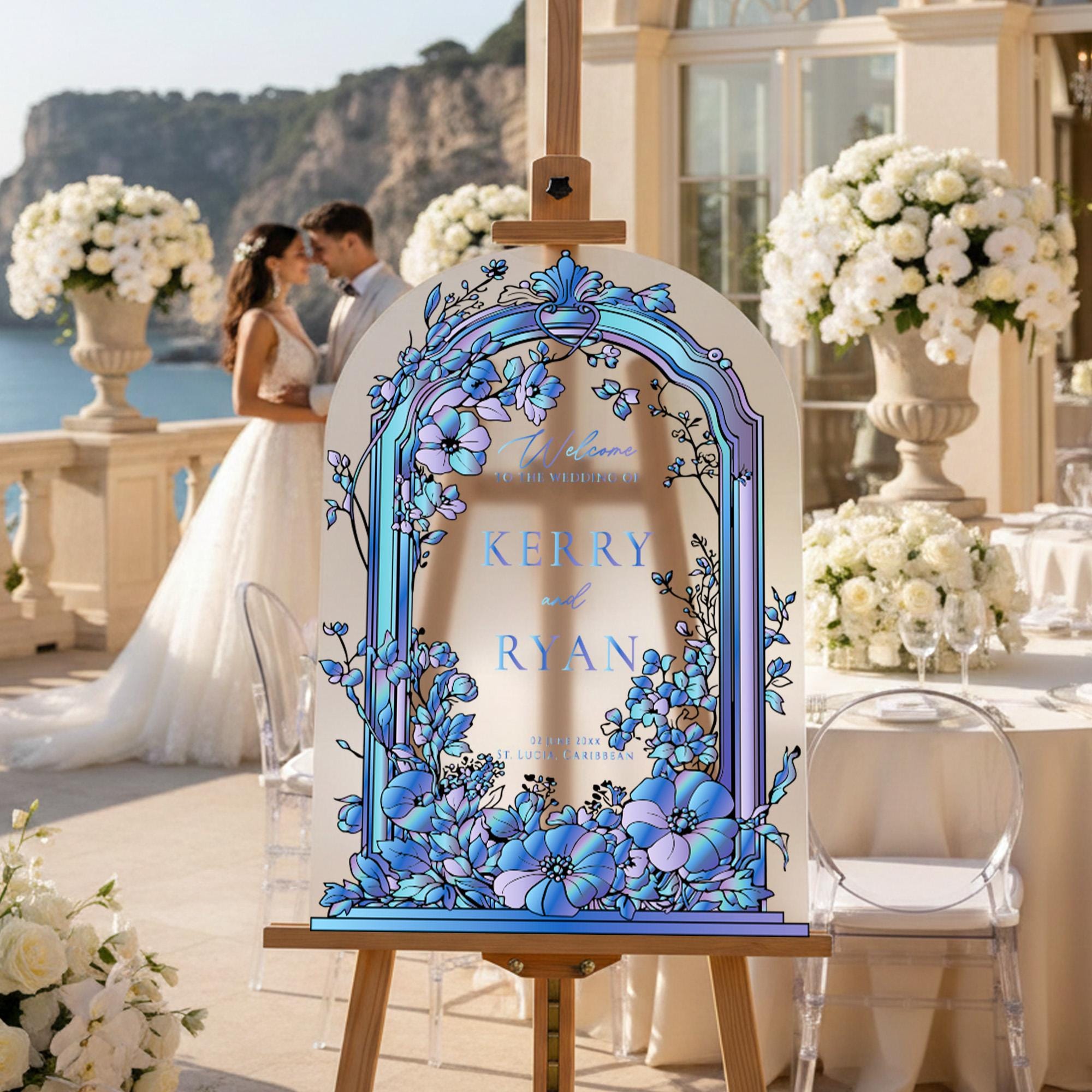 a couple standing on a balcony with a large floral arrangement in the background. In the foreground, there is a large sign with a floral design and text that reads "Kerry & Ryan".
