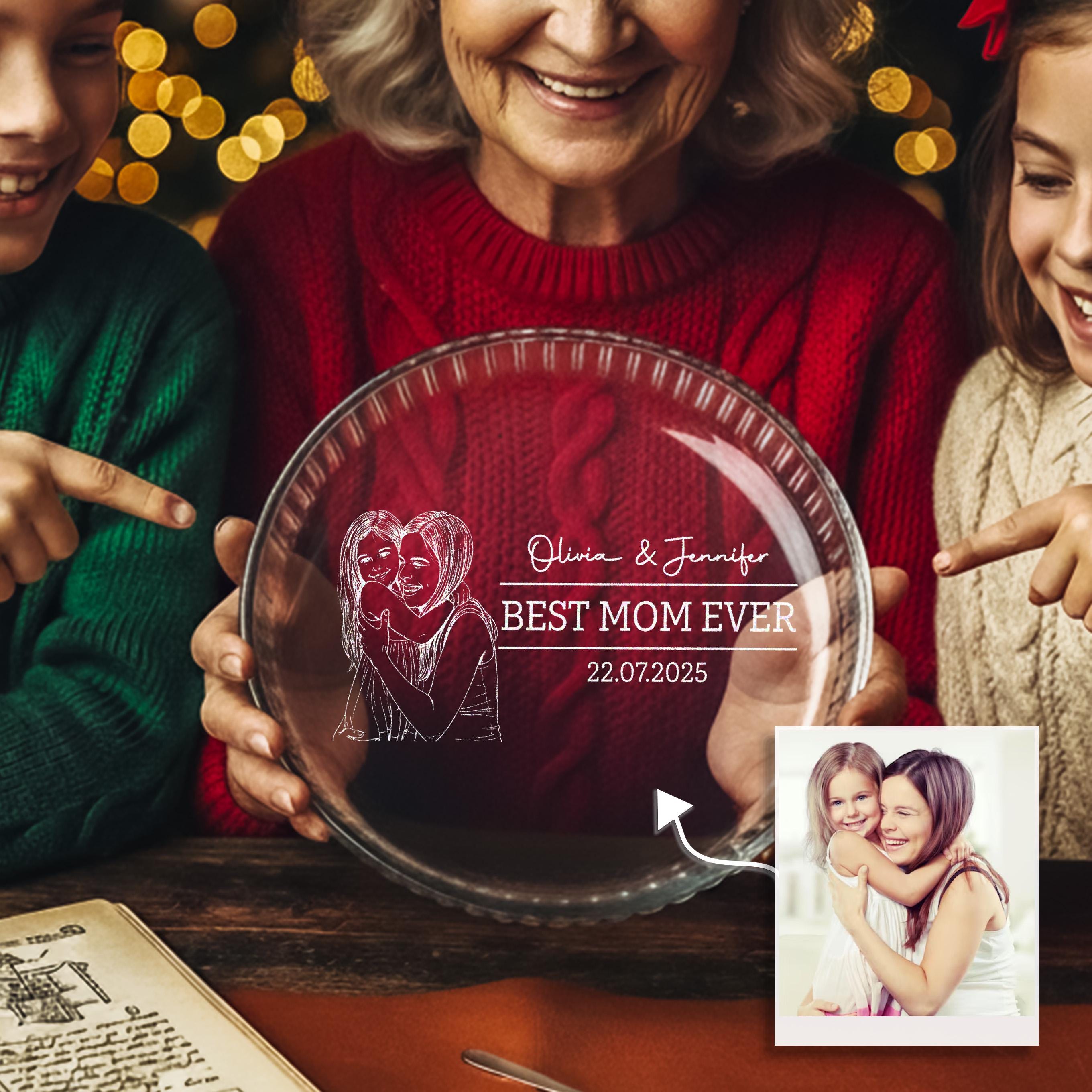 a woman holding a glass plate with a drawing of two women embracing, and the text "BEST MOM EVER 22.07.2025" written on it.