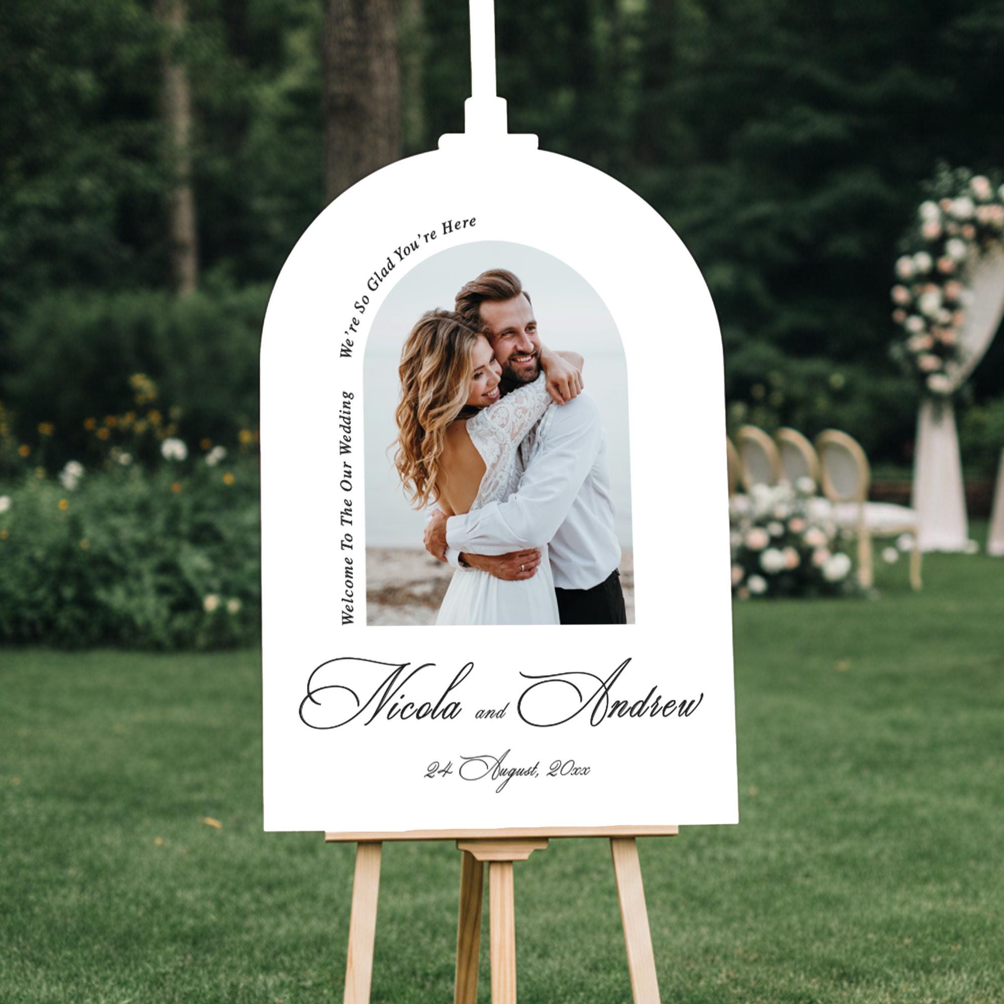 a white sign with a photo of a couple embracing, surrounded by text that reads "Welcome to the wedding of Nicola and Andrew" and "24th August, 20XX".