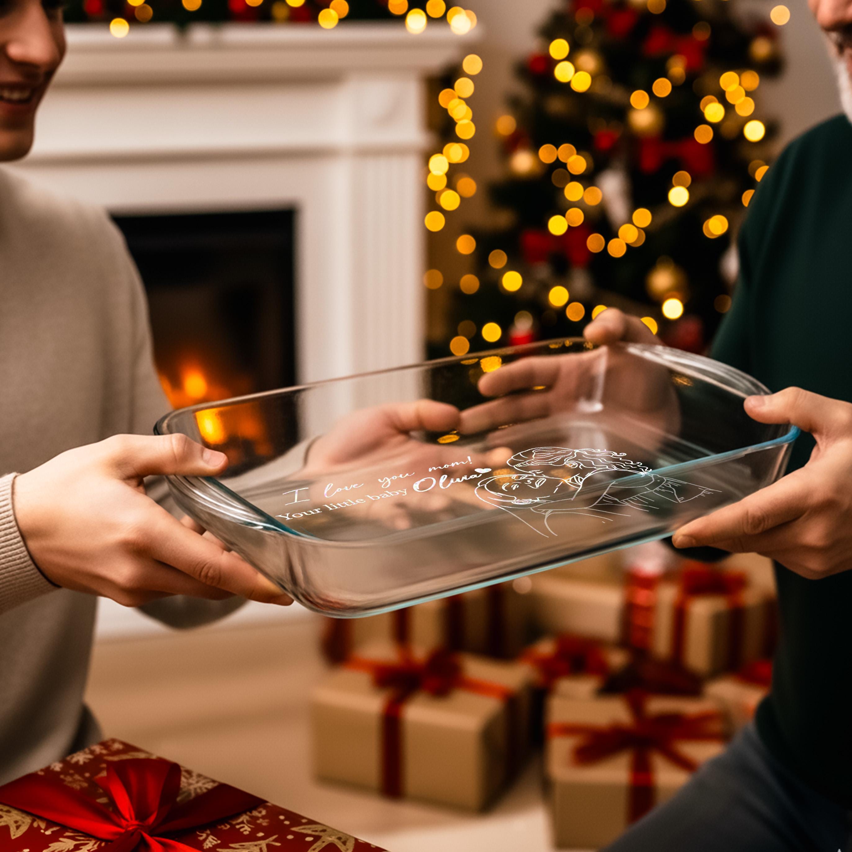 A person is holding a clear glass dish with a message written on it, while another person is holding a gift box with a red ribbon. In the background, there is a Christmas tree with twinkling lights.