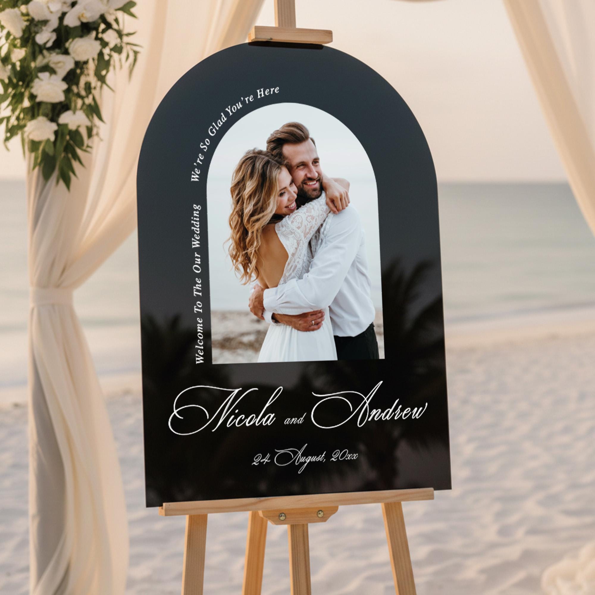 a couple embracing in a black arch-shaped sign with a beach and ocean in the background.