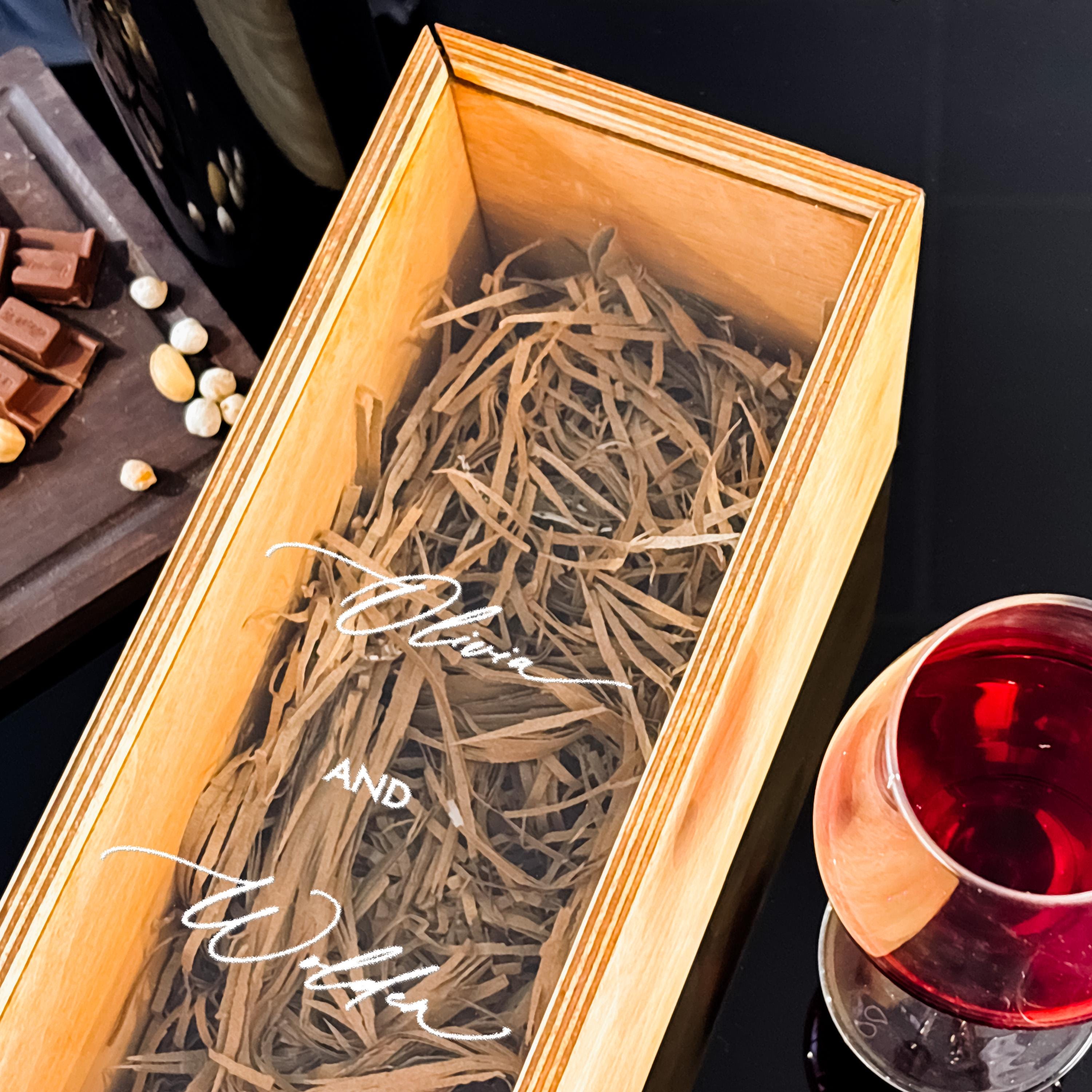 a wooden box with a glass of red wine and a plate of chocolate and nuts on a table.