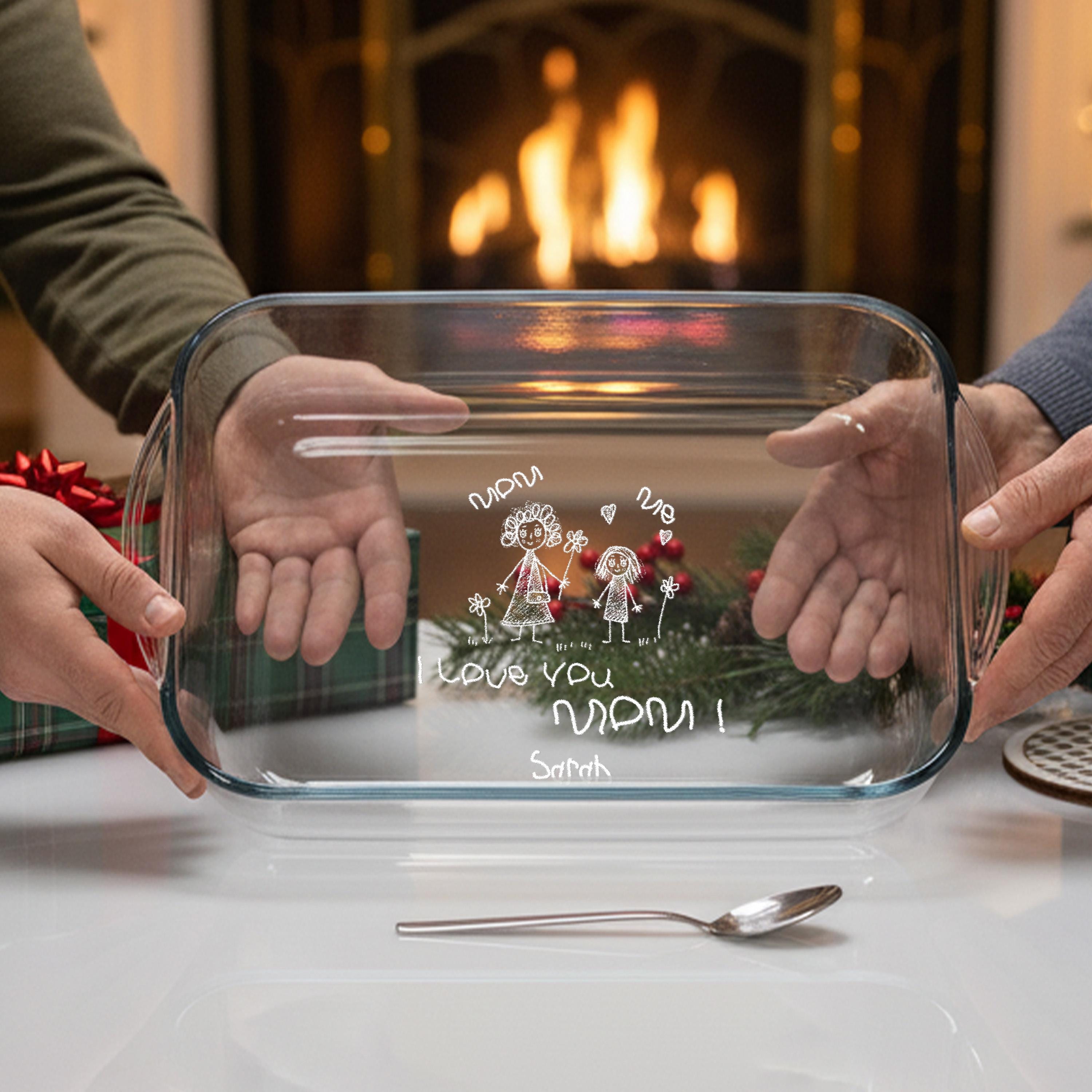 Two hands holding a clear glass casserole dish with a personalized message written on it.