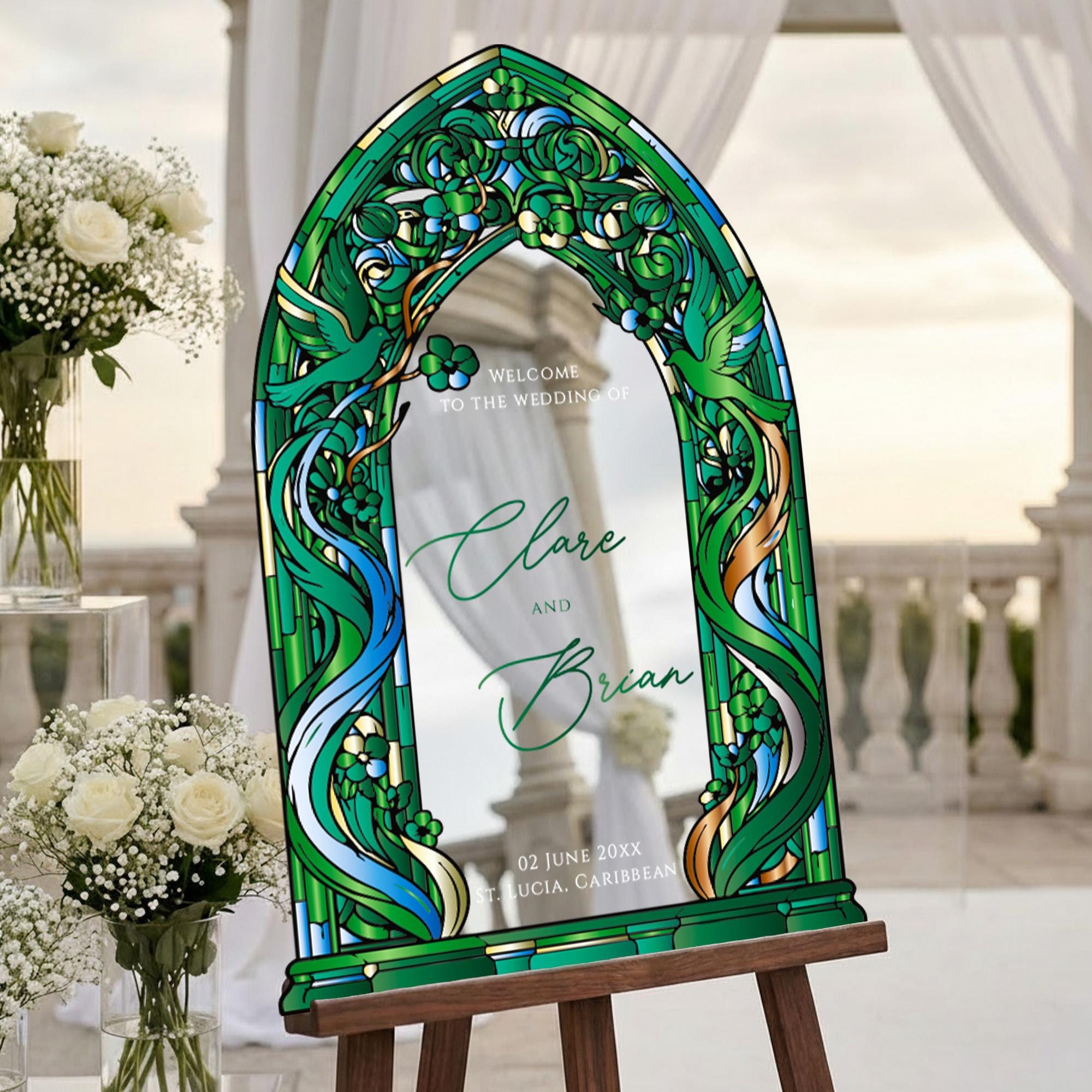 A large, ornate, green-framed sign displaying the names "Clare and Brian" and the date "02 JUNE 20XX" is set up in a garden or outdoor wedding venue.