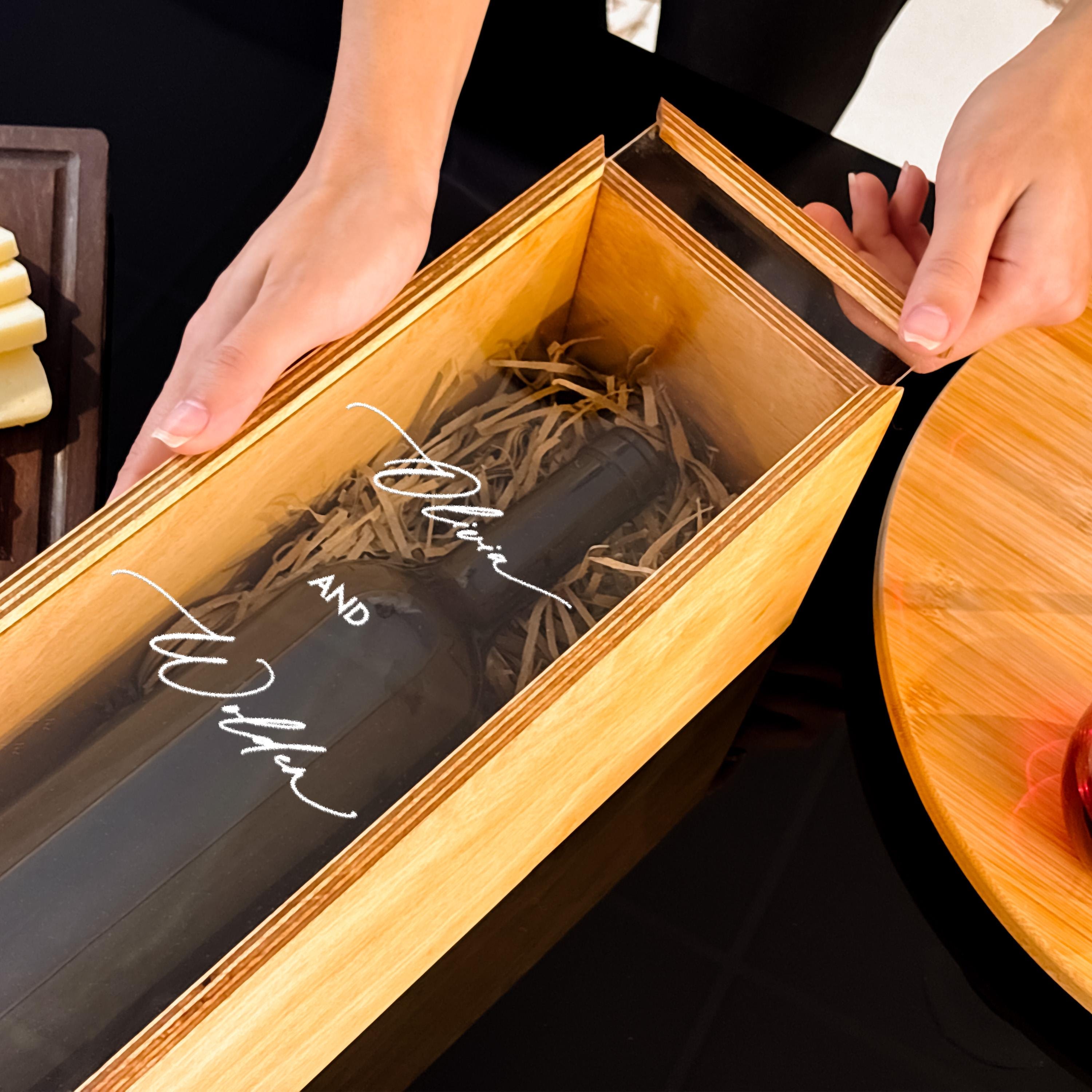 A person's hands are holding a wooden box containing a bottle of wine, with the label facing the viewer.