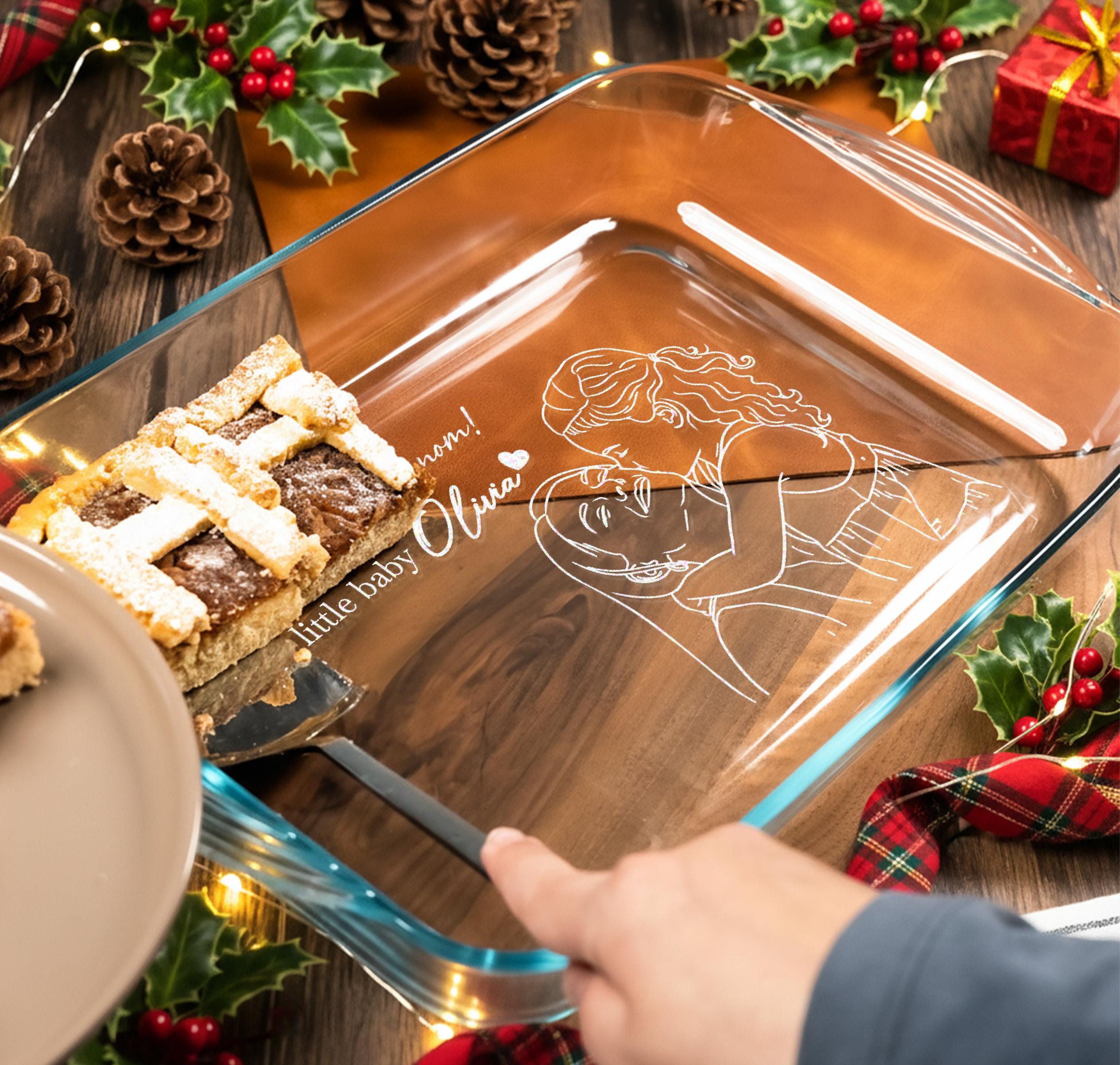 A person is holding a glass baking dish with a pie on it, surrounded by holiday decorations such as pine cones and holly leaves.