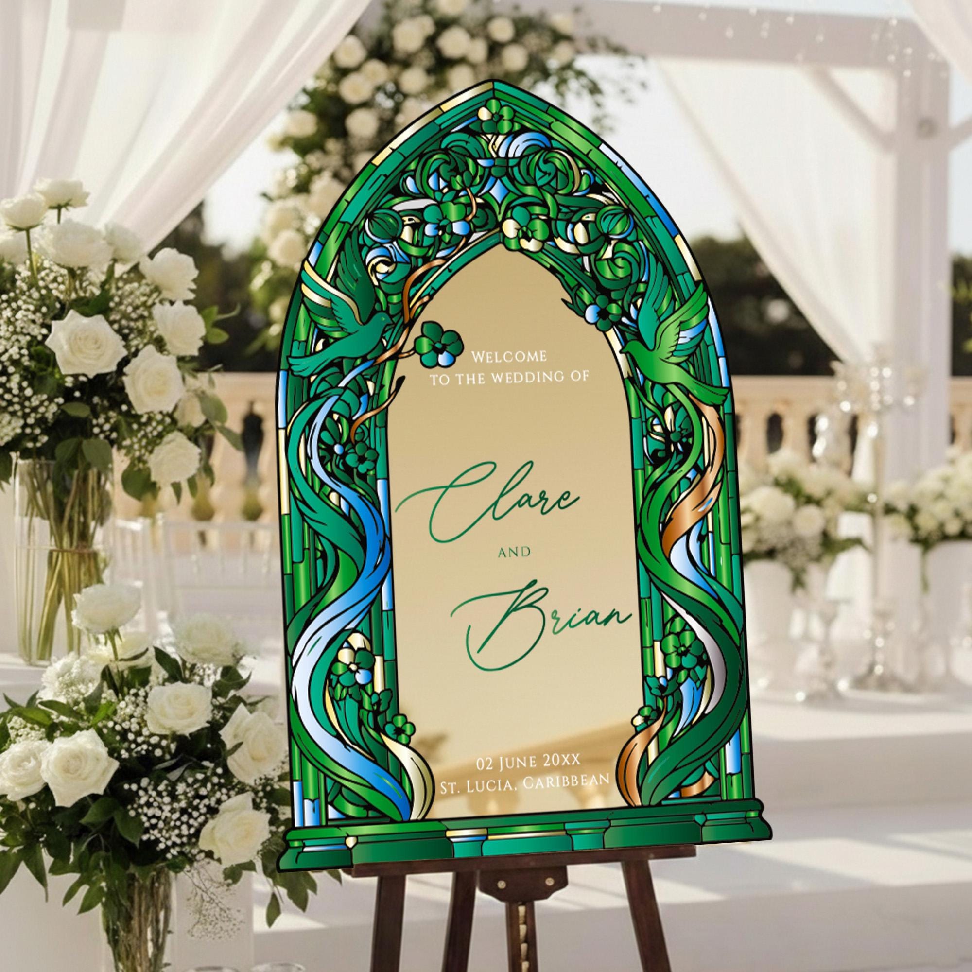 A stained glass-style wedding welcome sign with the names "Clare and Brian" and the date "12 June 2023" in the background, surrounded by white flowers and greenery.