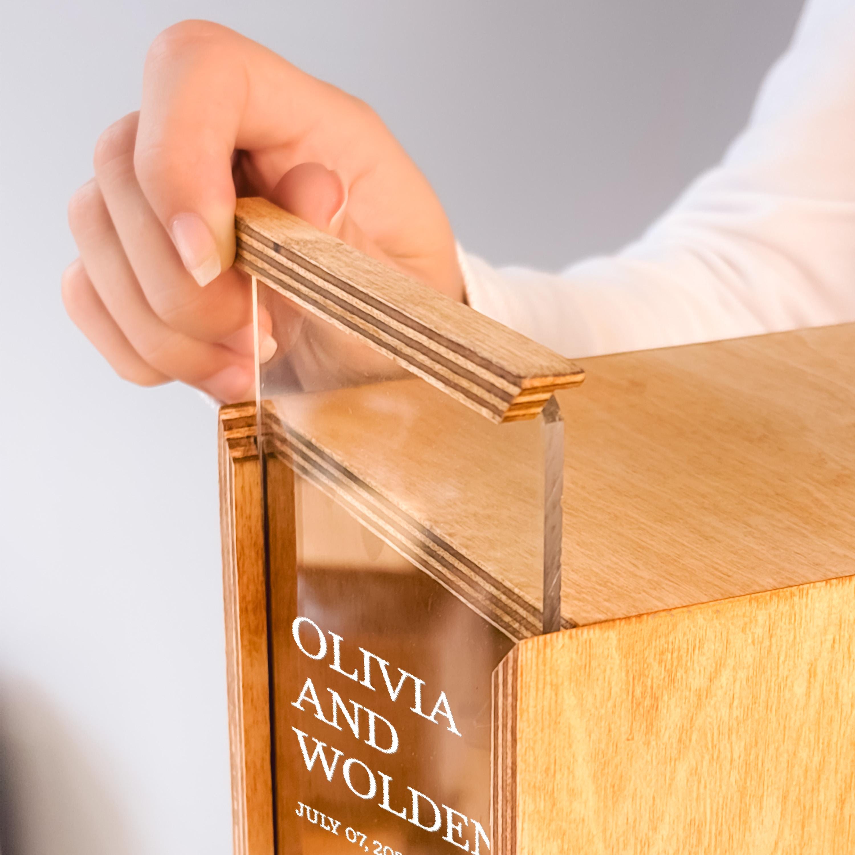A person's hand is holding a wooden object with a clear glass panel, which appears to be a wooden box or container.