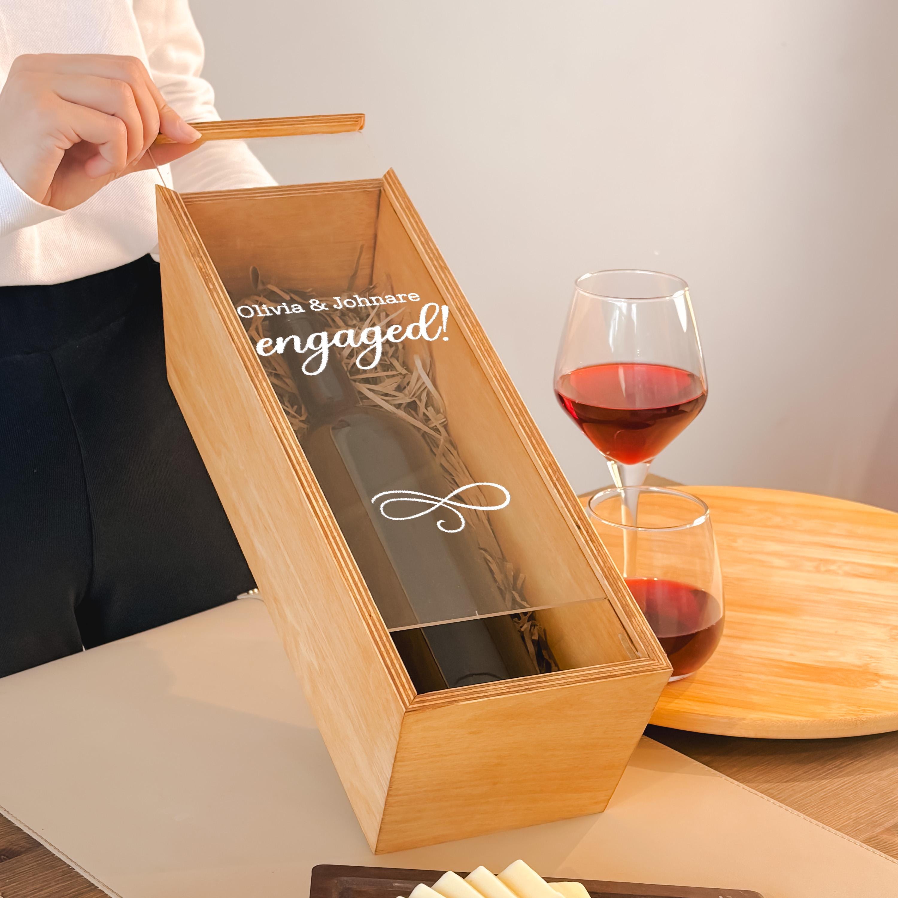 A person is holding a wooden box with a wine glass and a bottle of wine inside it, suggesting a celebration or special occasion.