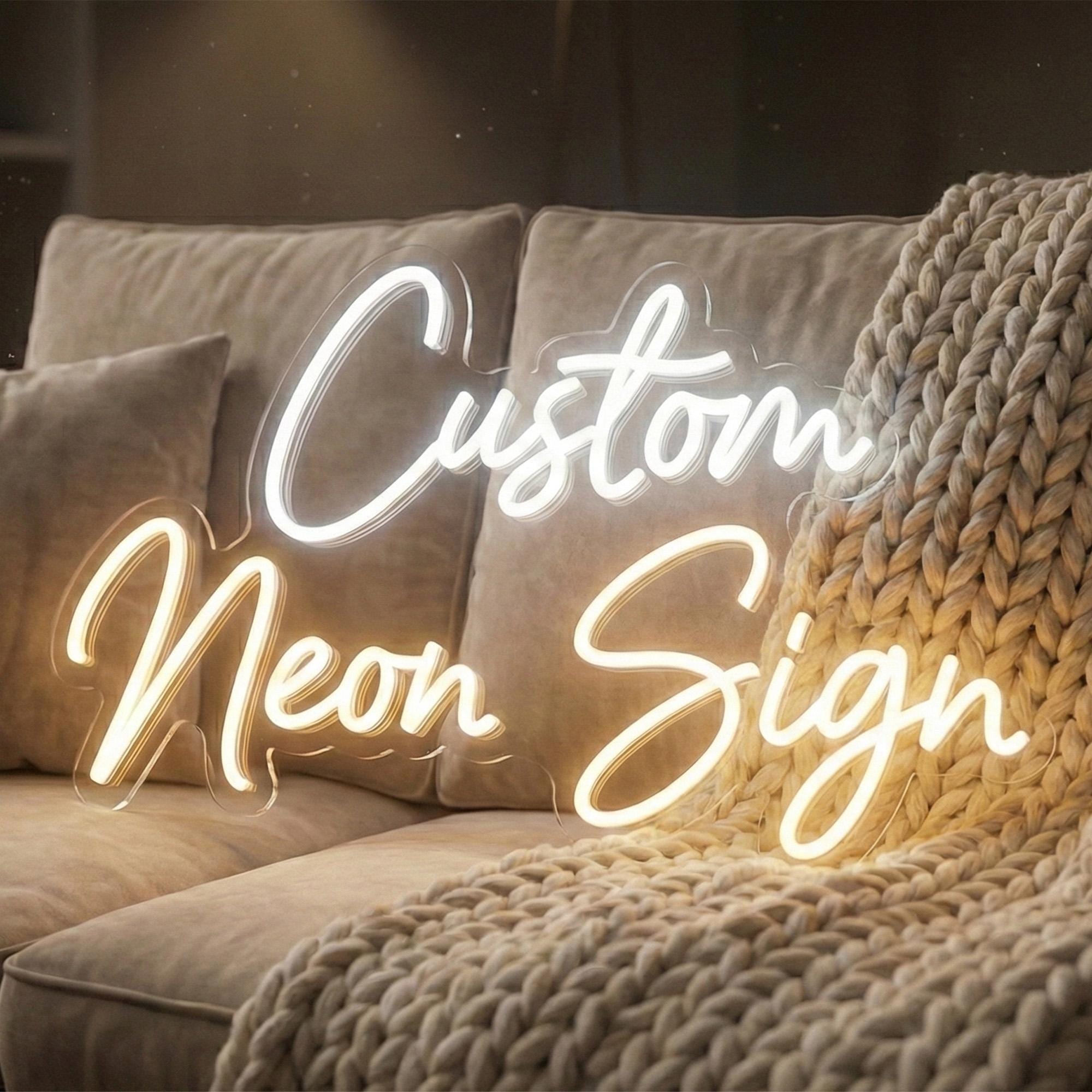 a cozy living space with a plush couch and a warm, textured blanket. The couch is adorned with a beige pillow, and a blanket is draped over it. The image also contains the text "Custom Neon Sign" in a cursive font, which appears to be a decorative element in the room