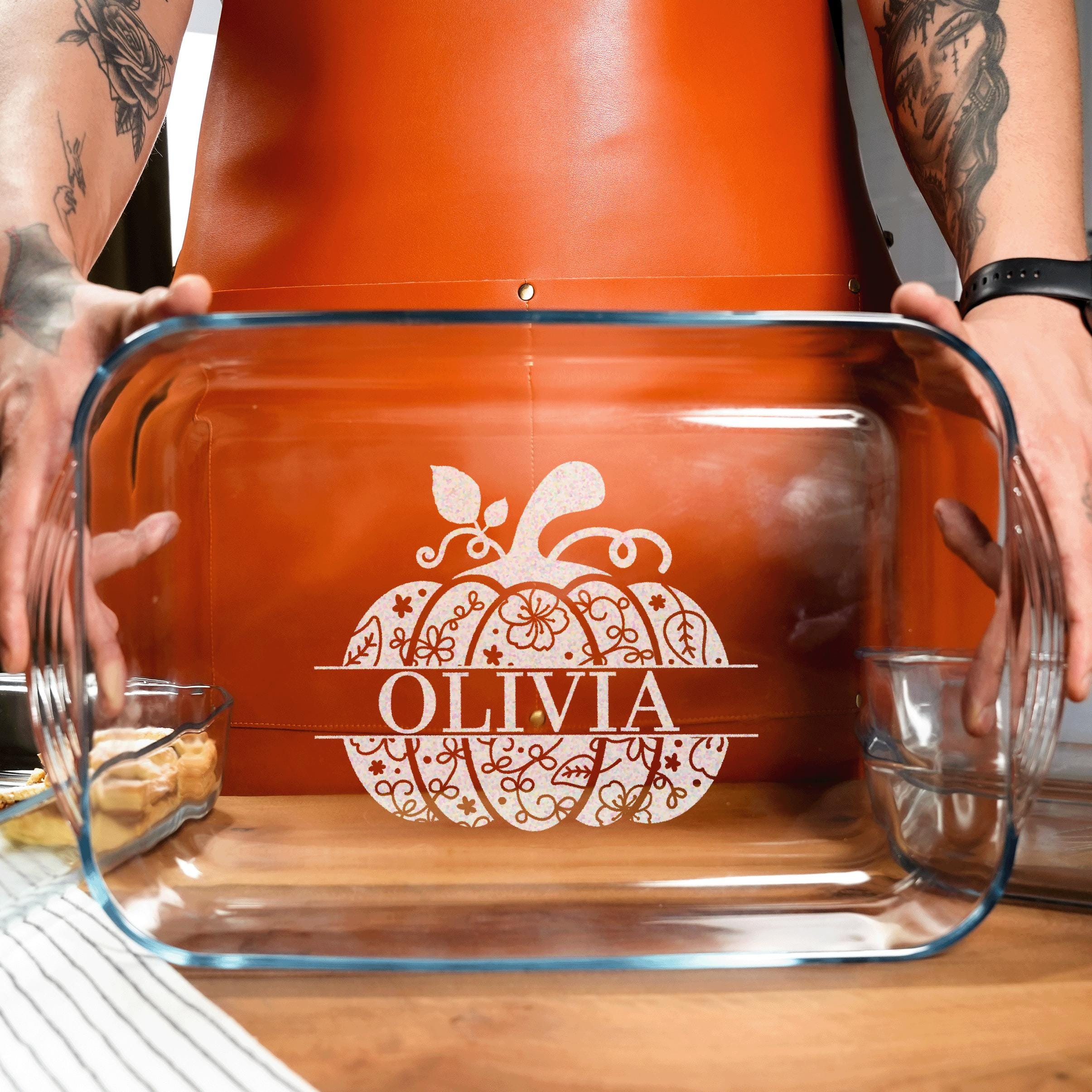 A person is holding a clear glass casserole dish with a pumpkin design and the name "OLIVIA" printed on it.