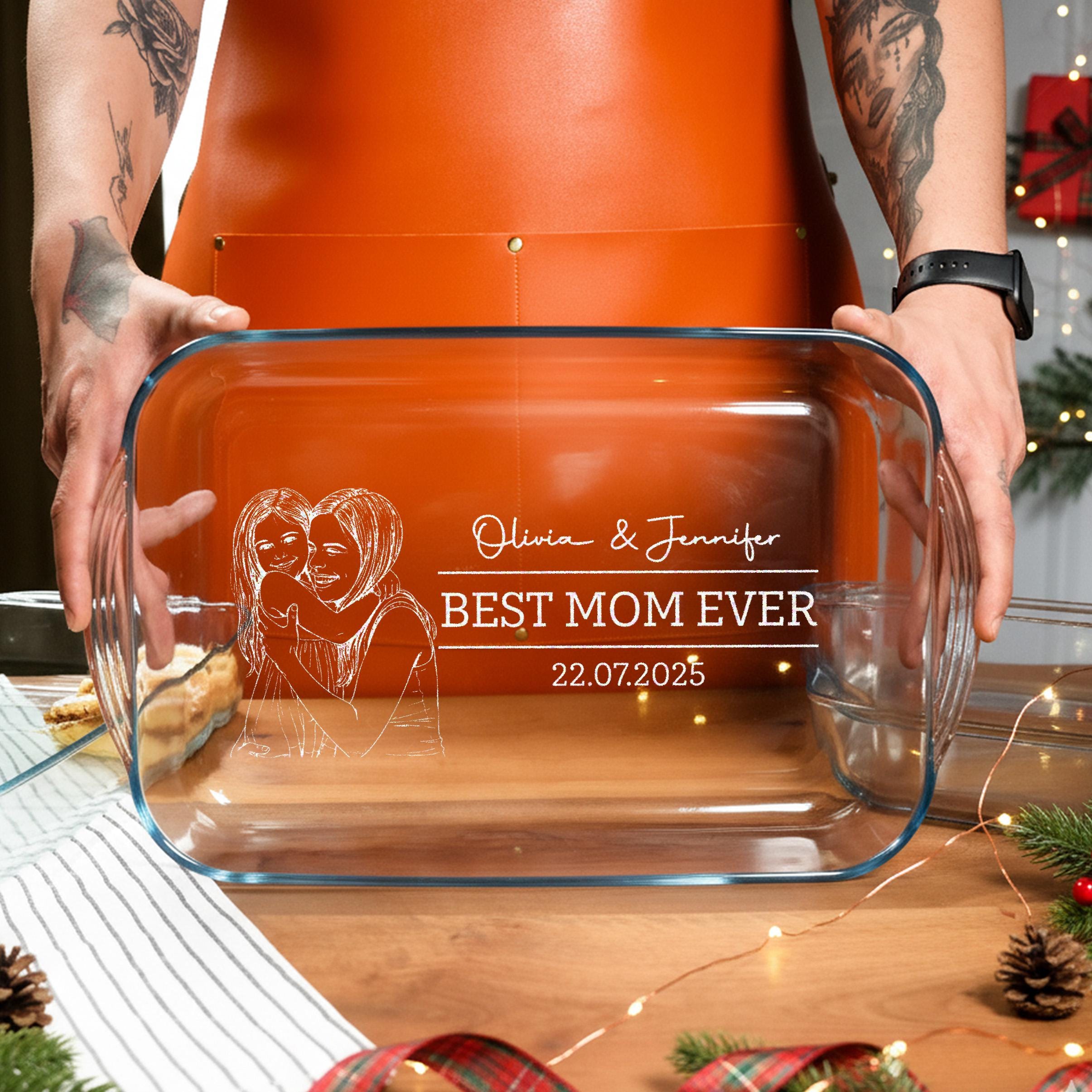 A person is holding a clear glass casserole dish with a personalized message engraved on it.