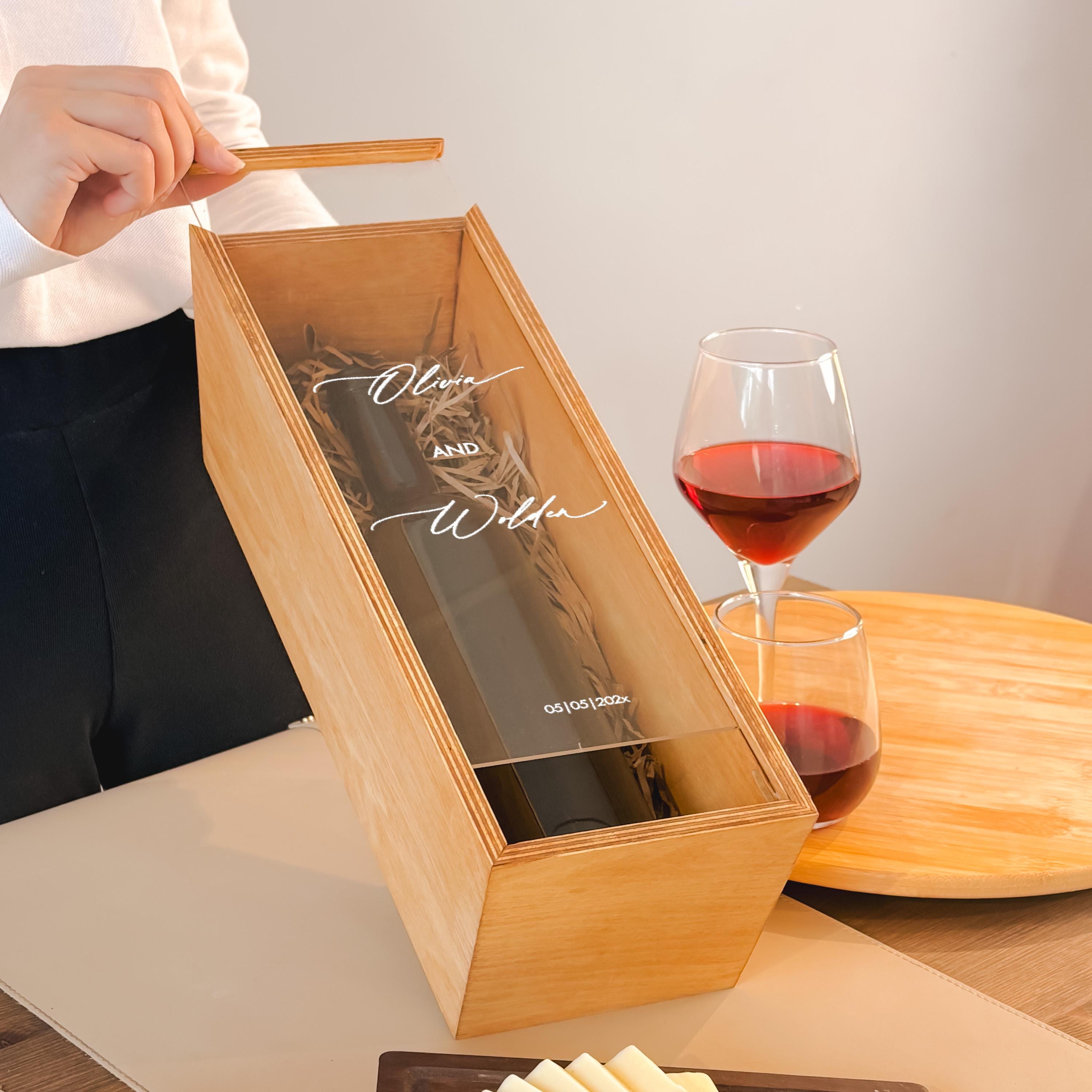 A person is holding a wooden box with a glass of red wine and cheese on a wooden table.