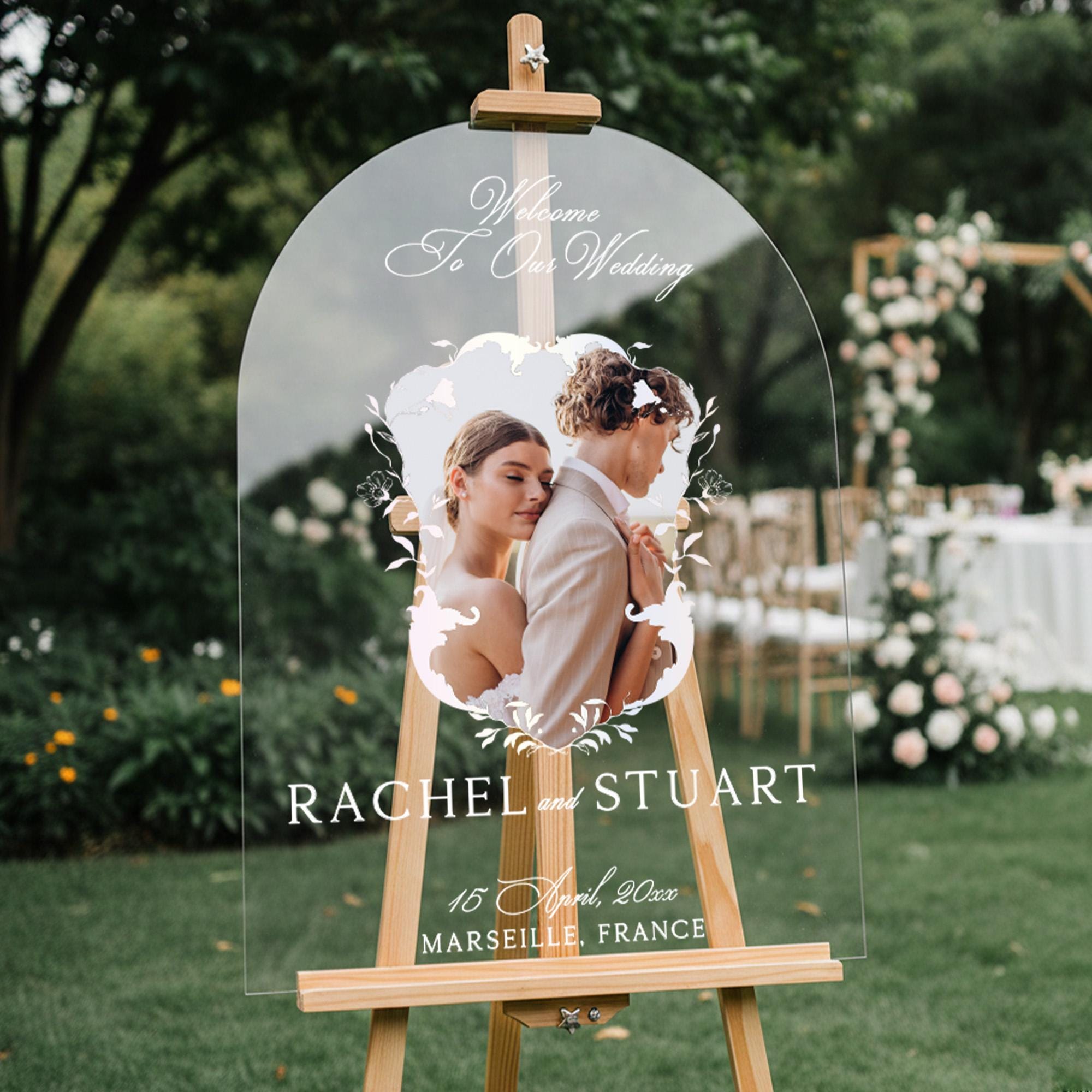 a clear wooden easel displaying a wedding welcome sign with a photo of a couple embracing.