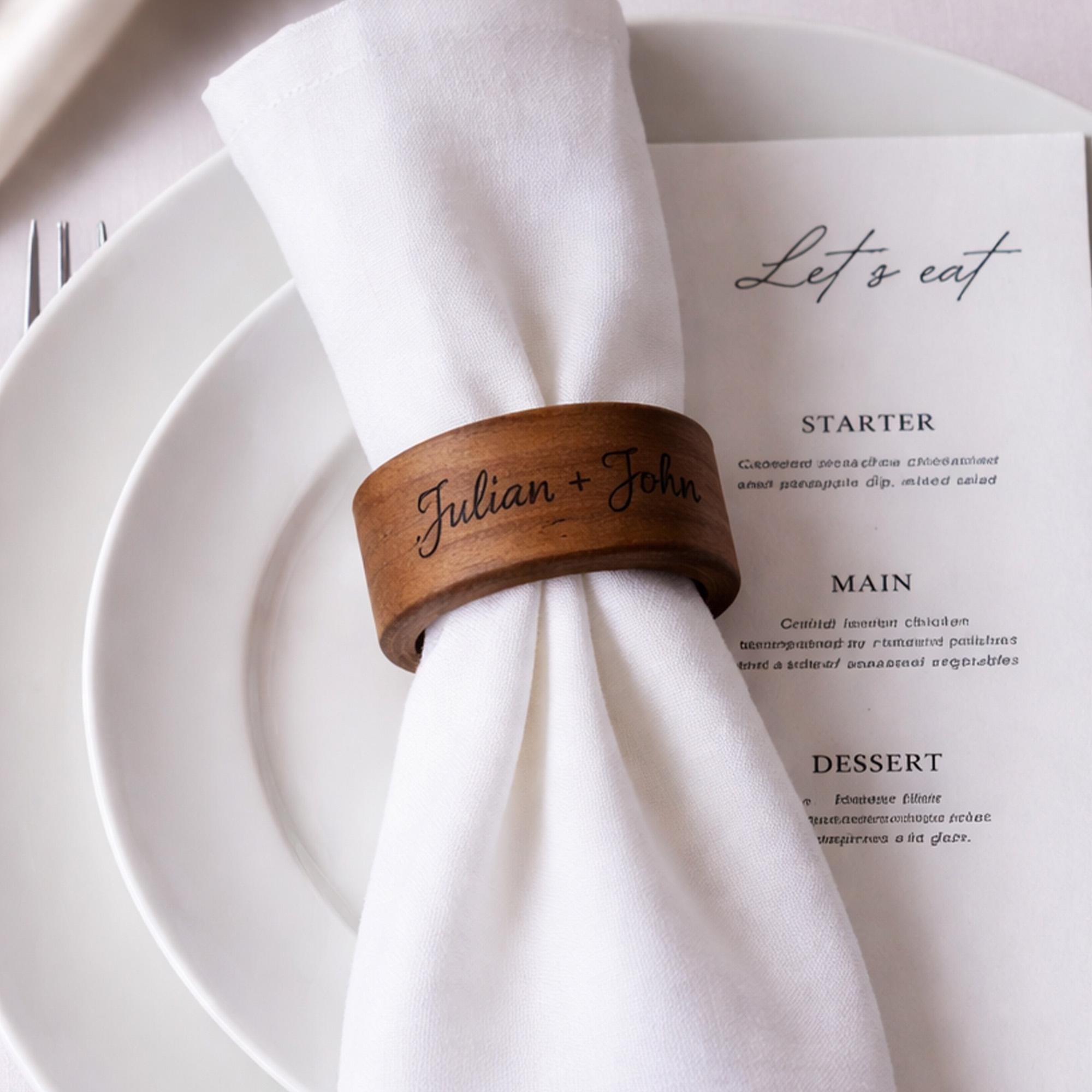 Personalized wooden napkin ring engraved with couple names, elegant wedding table setting with white linen and minimalist plates