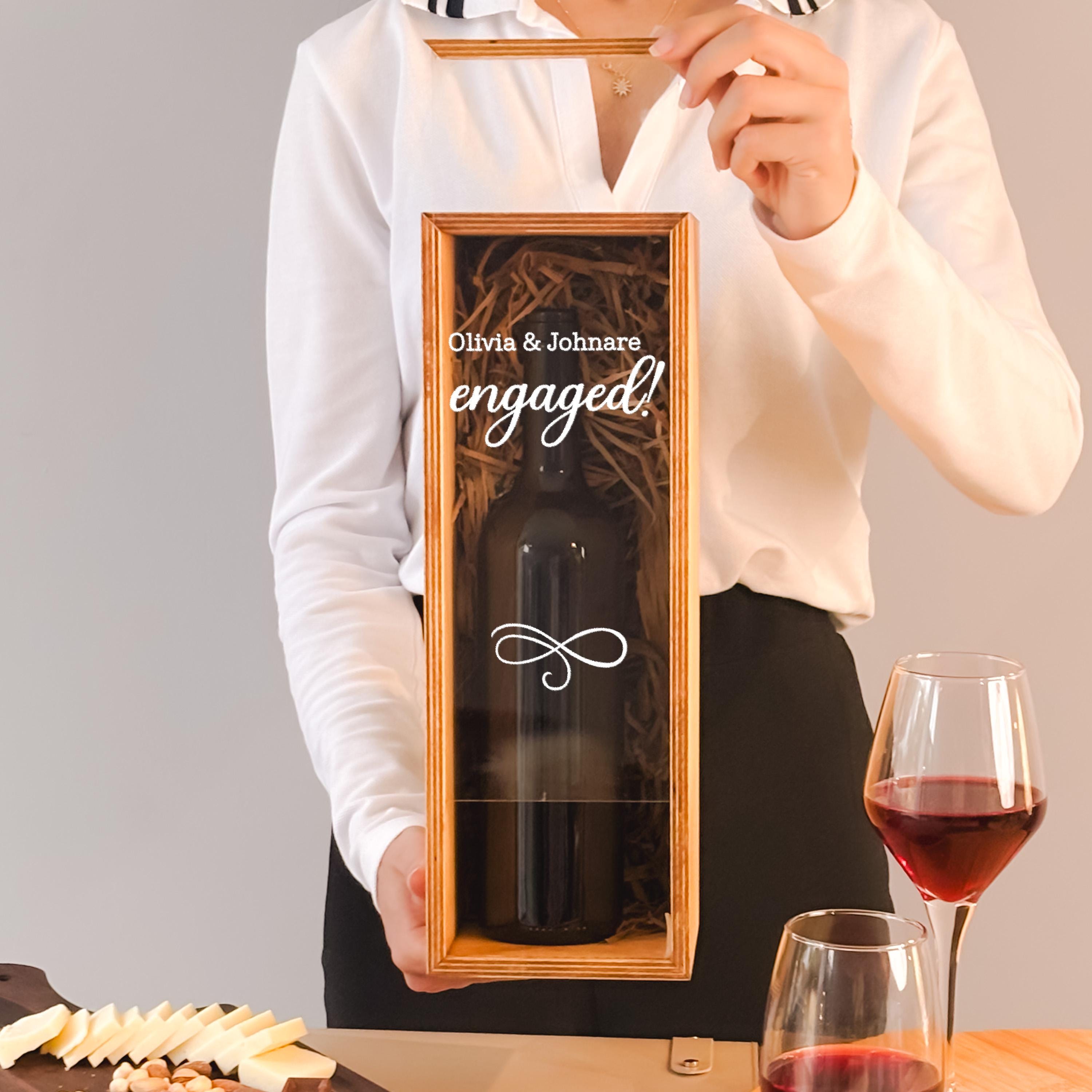 A person is holding a wine bottle in a wooden box, with a glass of red wine and cheese on a table in front of them.