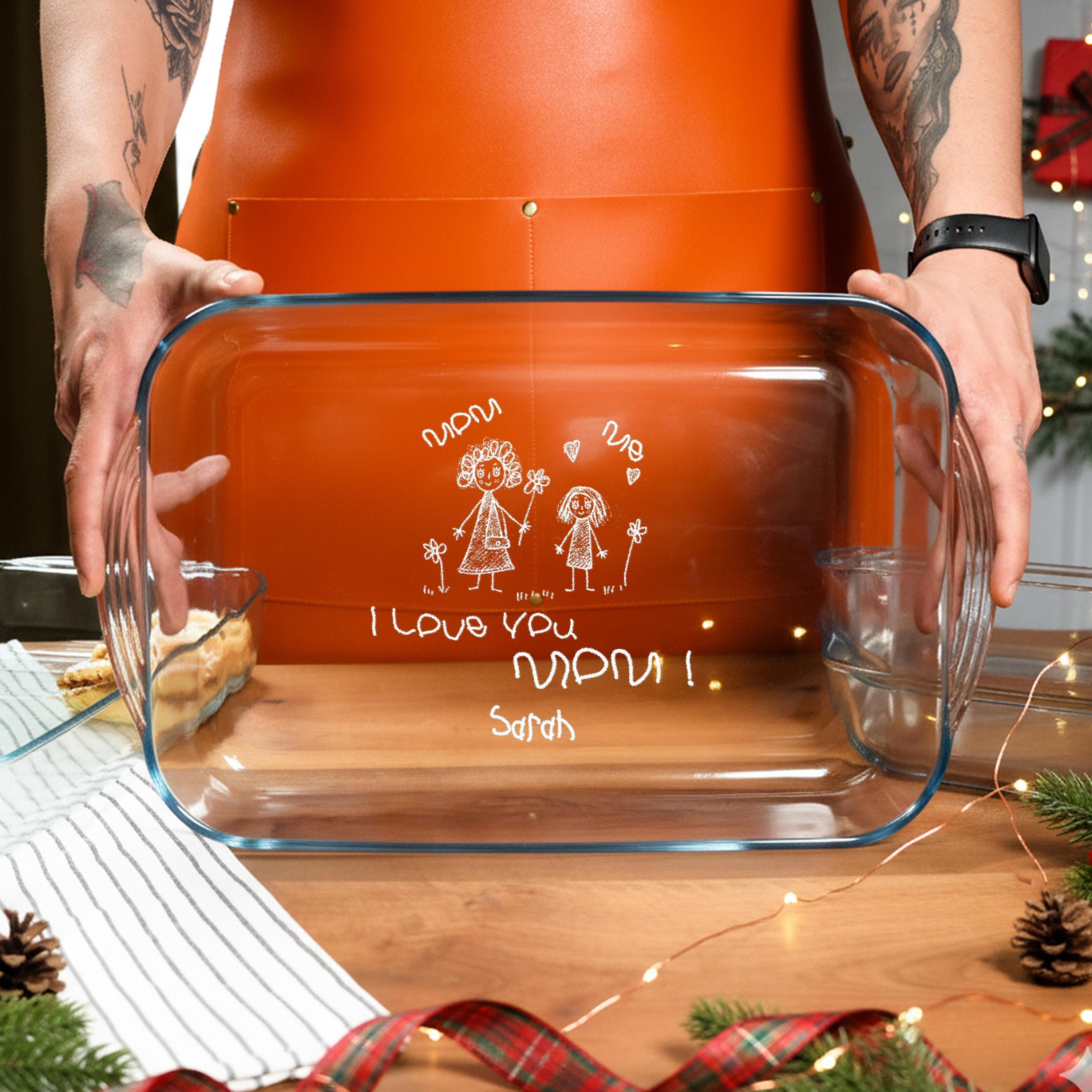 A person is holding a clear glass casserole dish with a personalized message written on it.