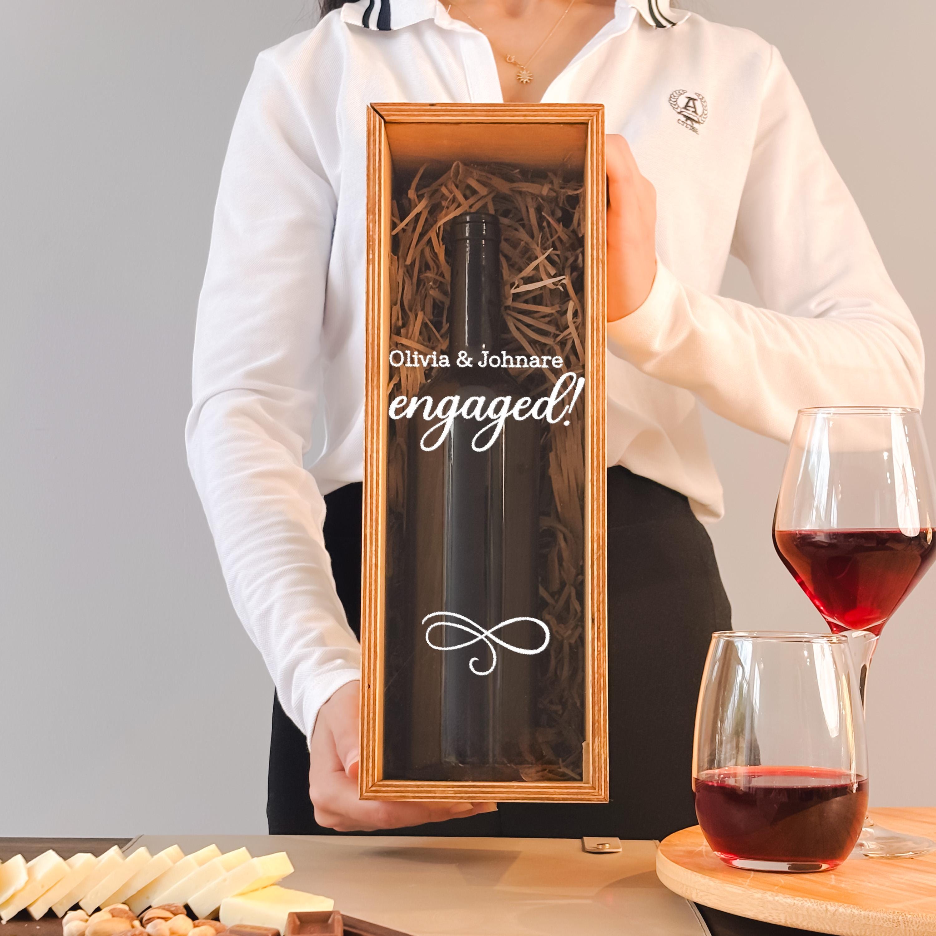 A person is holding a wine bottle in a wooden box, with a glass of red wine and cheese in front of them.