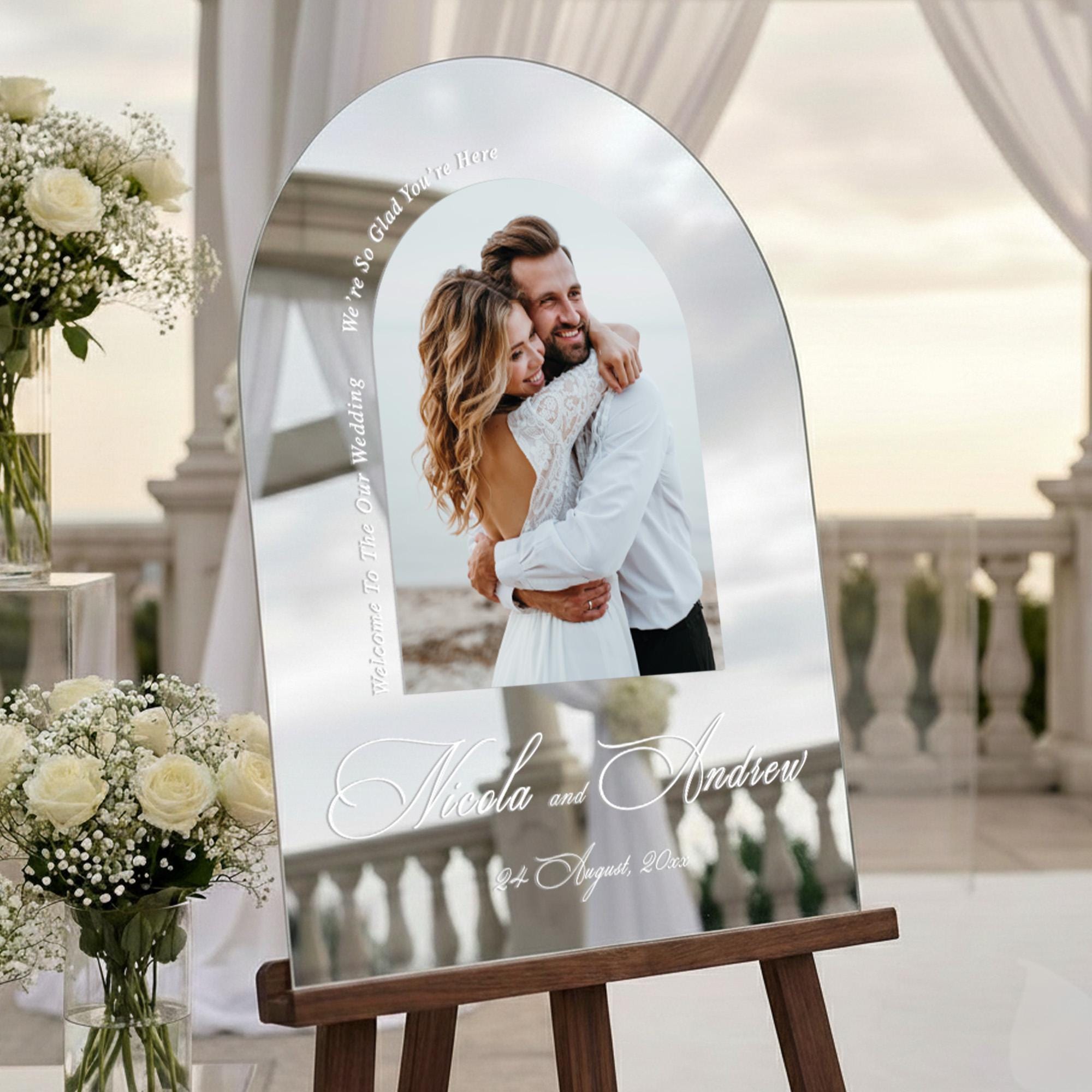 a wedding invitation stand with a photo of a couple embracing, surrounded by white flowers and a white curtain.
