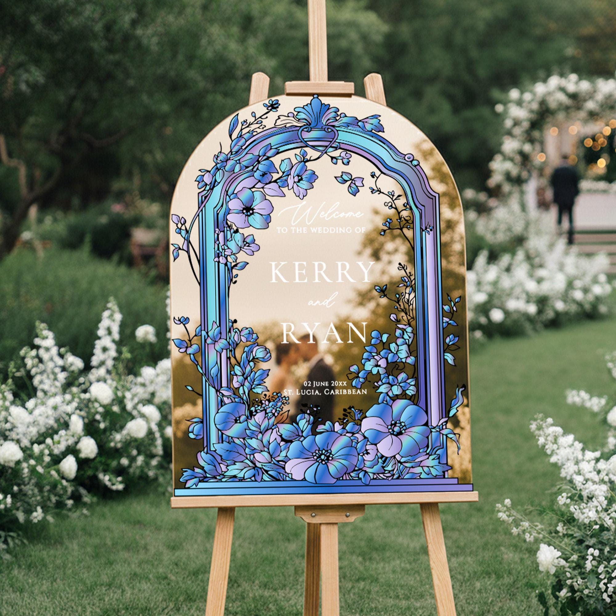 A wooden sign with a floral design, displaying the names 'Kerry' and 'Ryan', in a garden setting with white flowers and greenery in the background.
