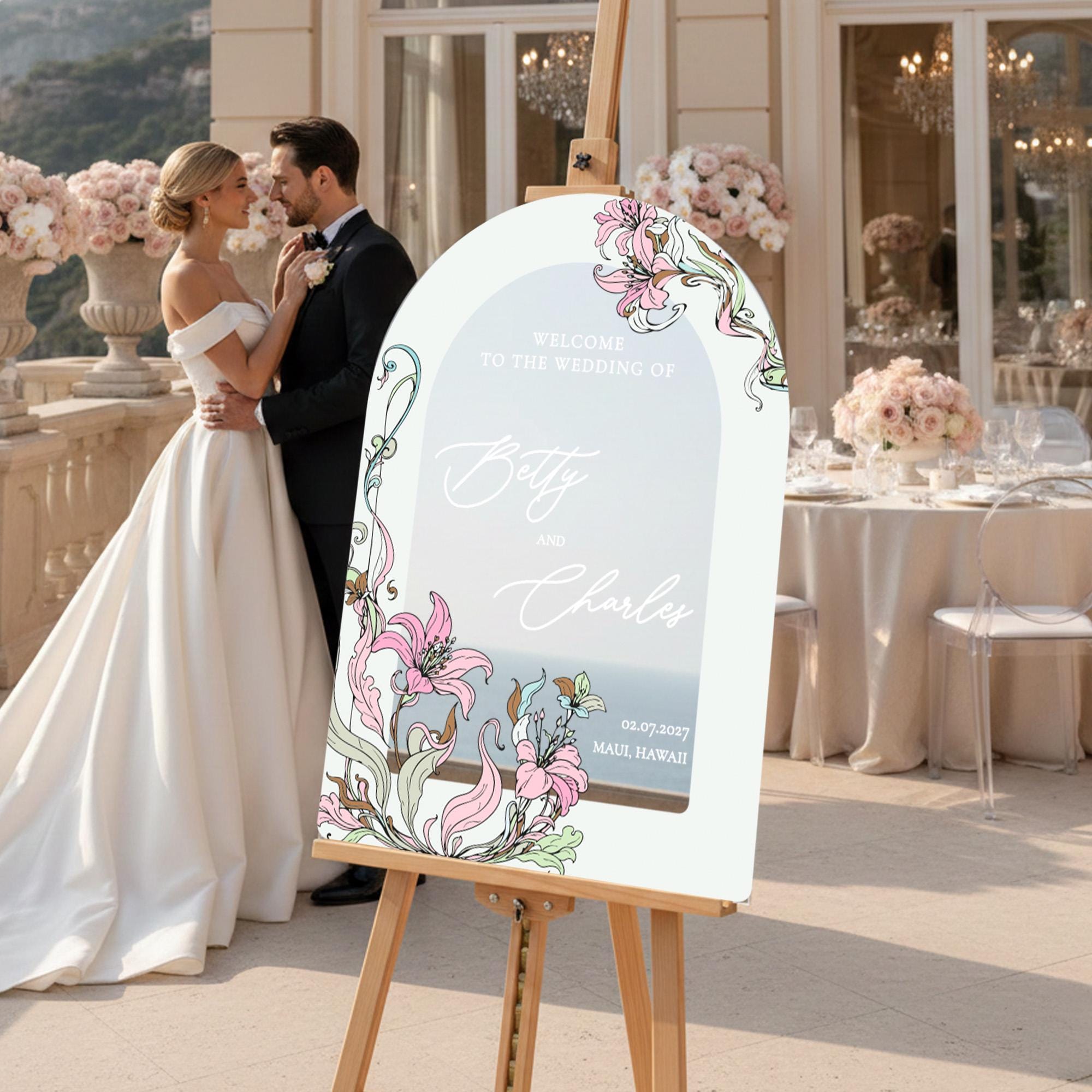 A bride and groom stand in front of a wedding sign that reads "Welcome to the Wedding of Betty and Charles 02.07.2017 Maui, Hawaii".