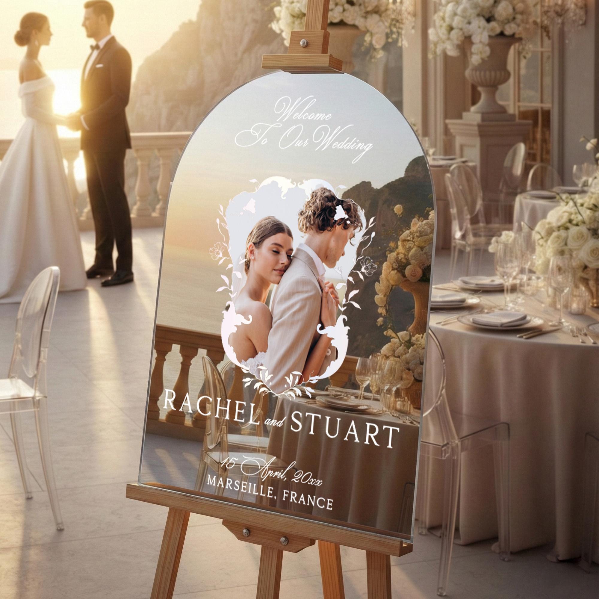 a wedding invitation board with a couple embracing in the center, surrounded by a scenic backdrop. The text on the board reads "Welcome to Our Wedding" and "RACHEL and STUART".