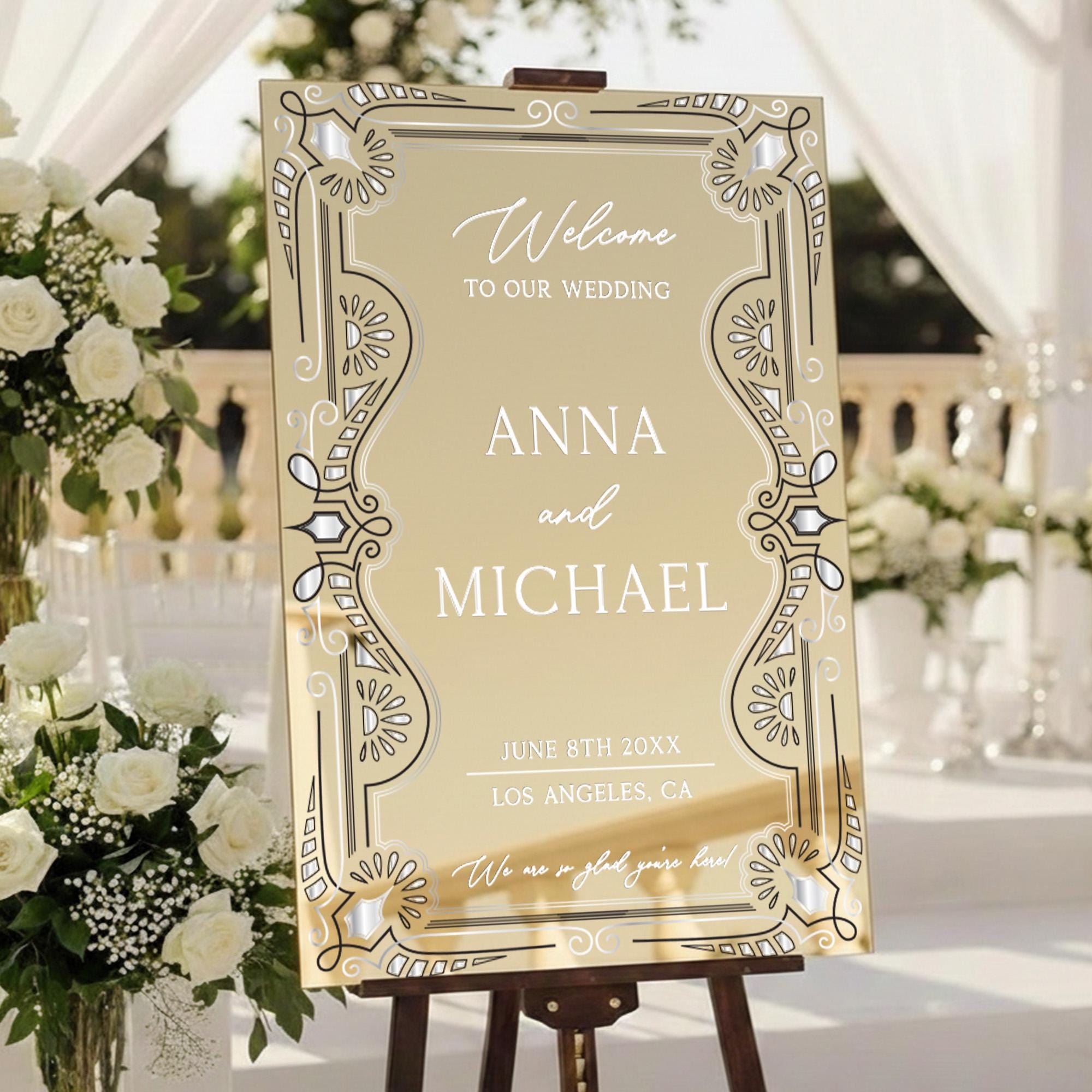A wedding welcome sign with the names 'Anna and Michael' on it, placed in a garden setting with white flowers and a gazebo in the background.