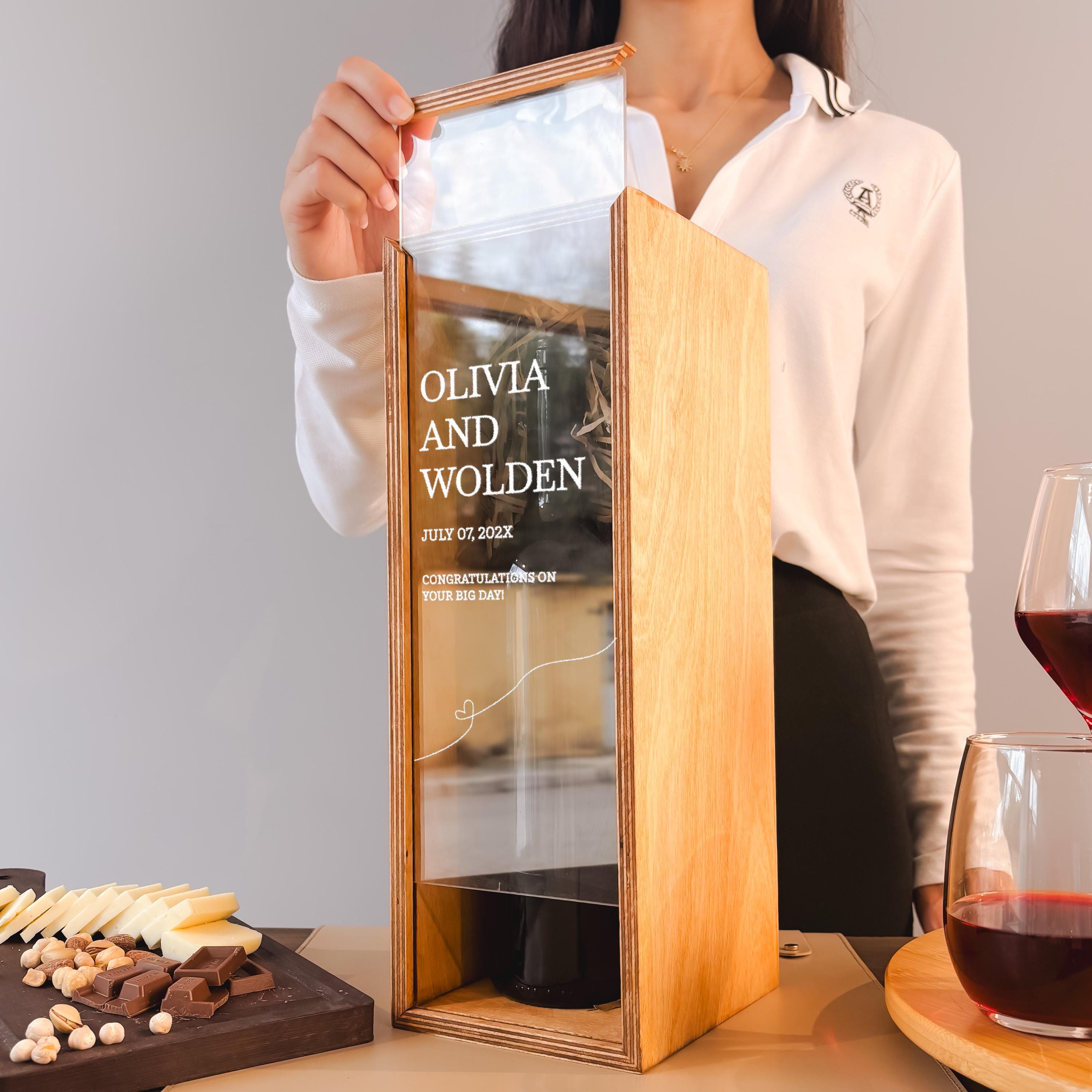A person is holding a wooden box with text on it, standing next to a table with food and drinks.