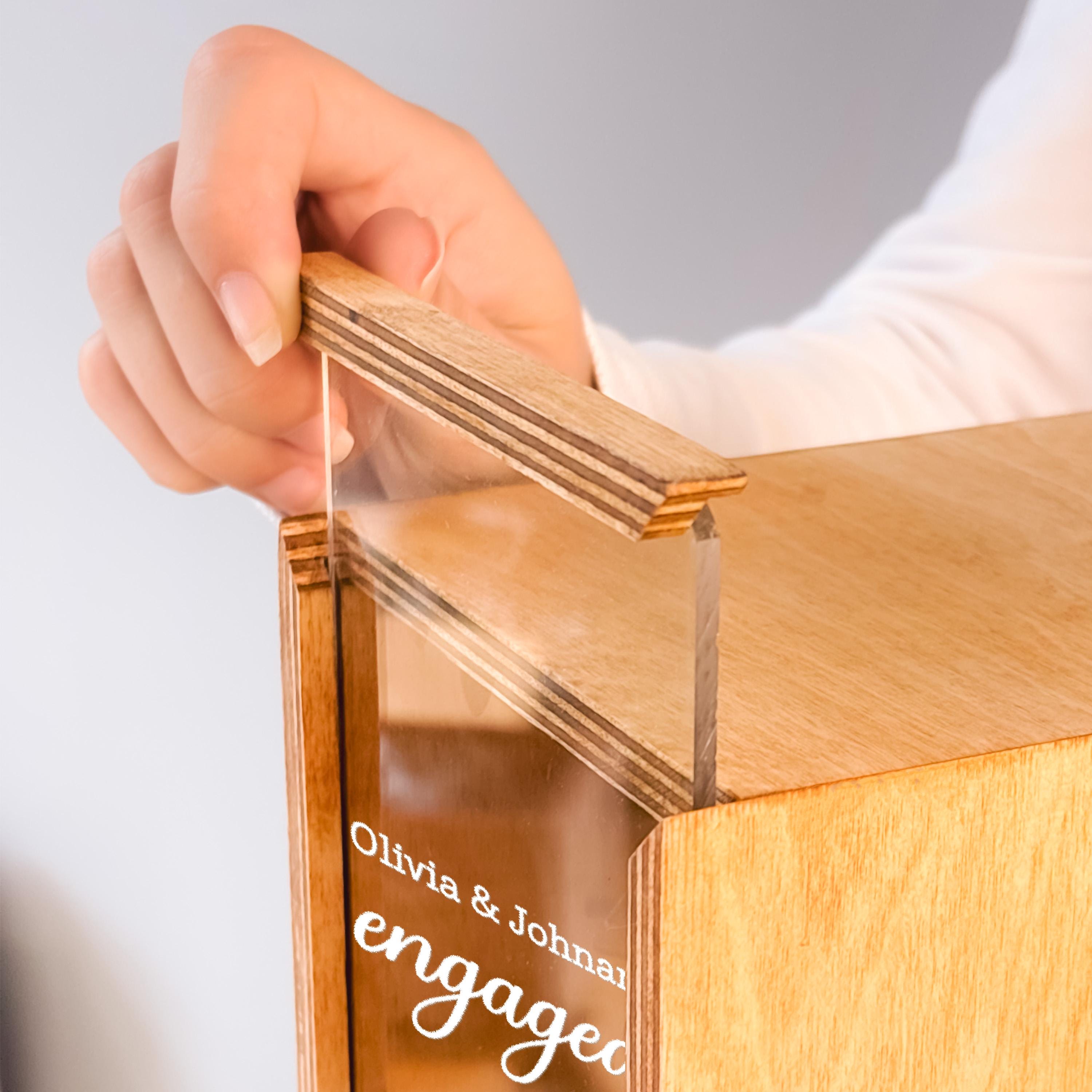 A person's hand is holding a wooden object with a clear glass panel, which appears to be a wooden box or container.