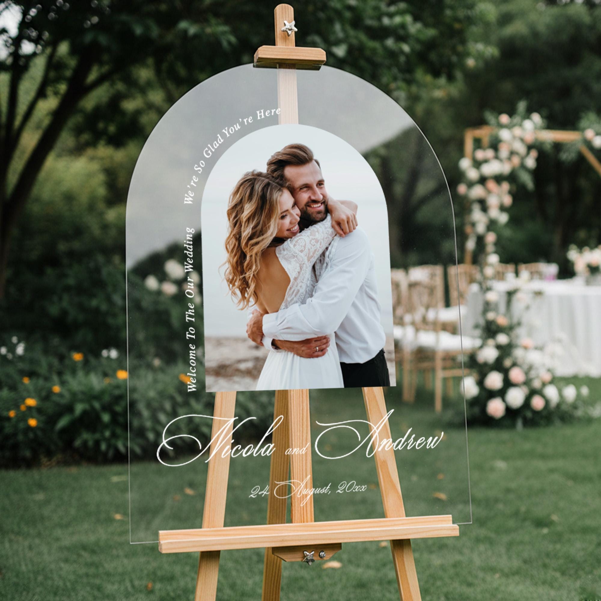 a couple embracing in a garden setting, with a wooden easel displaying a photo of them.
