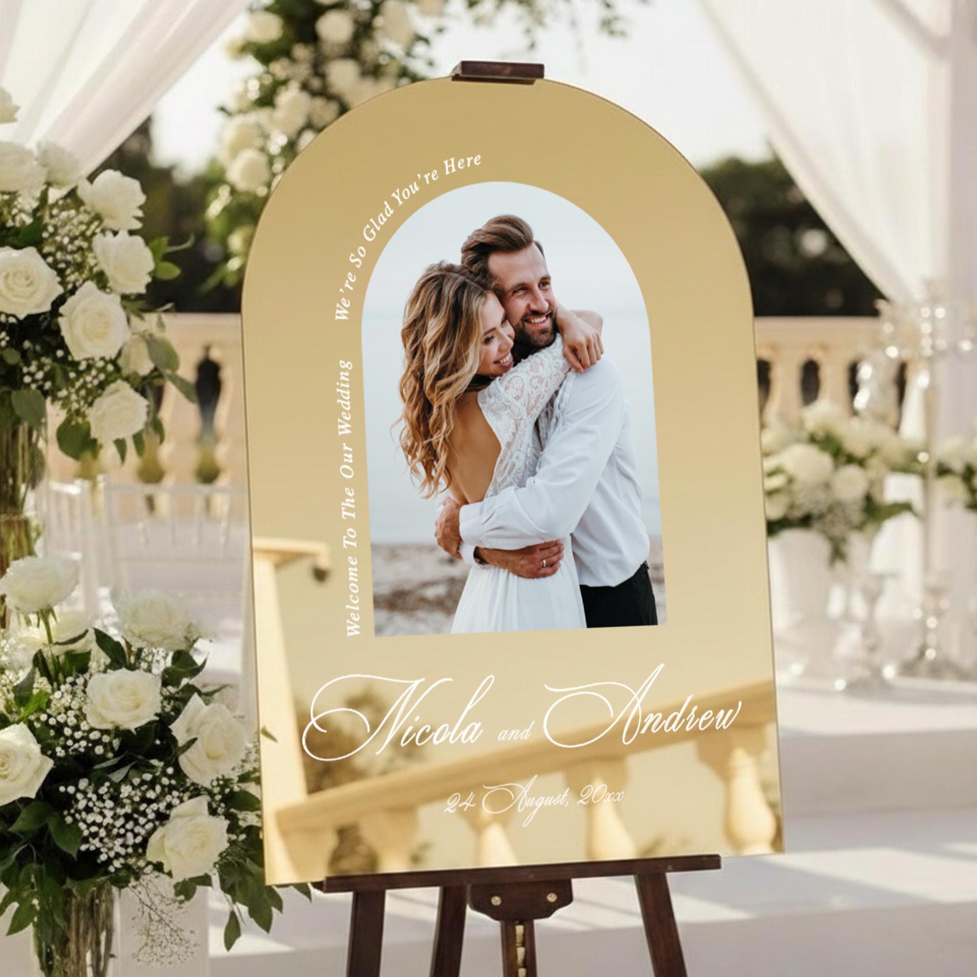 a wedding invitation sign with a couple embracing in the center, surrounded by white flowers and greenery.