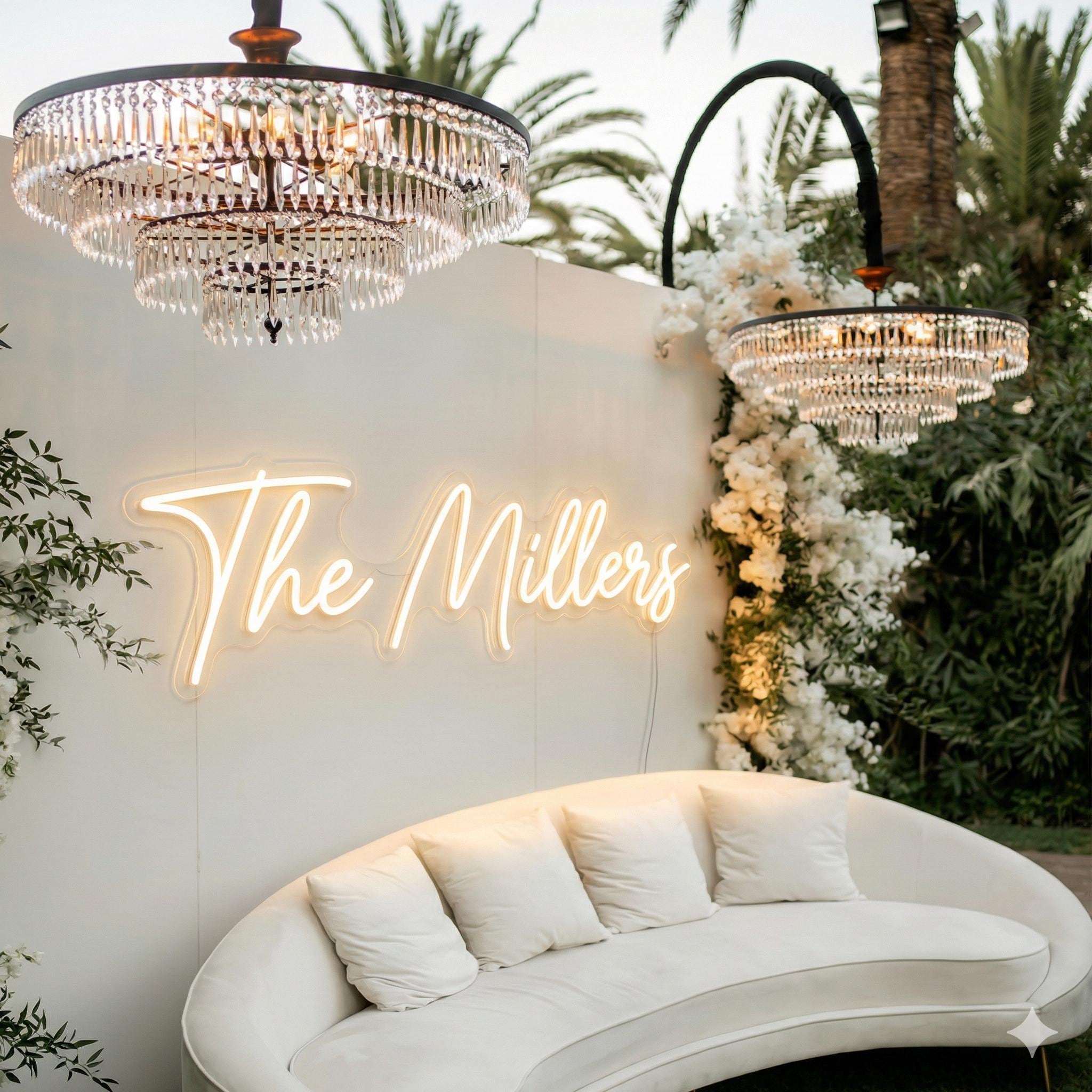 a white sofa with a neon sign that reads "The Millers" in front of a tropical garden setting with palm trees and white flowers