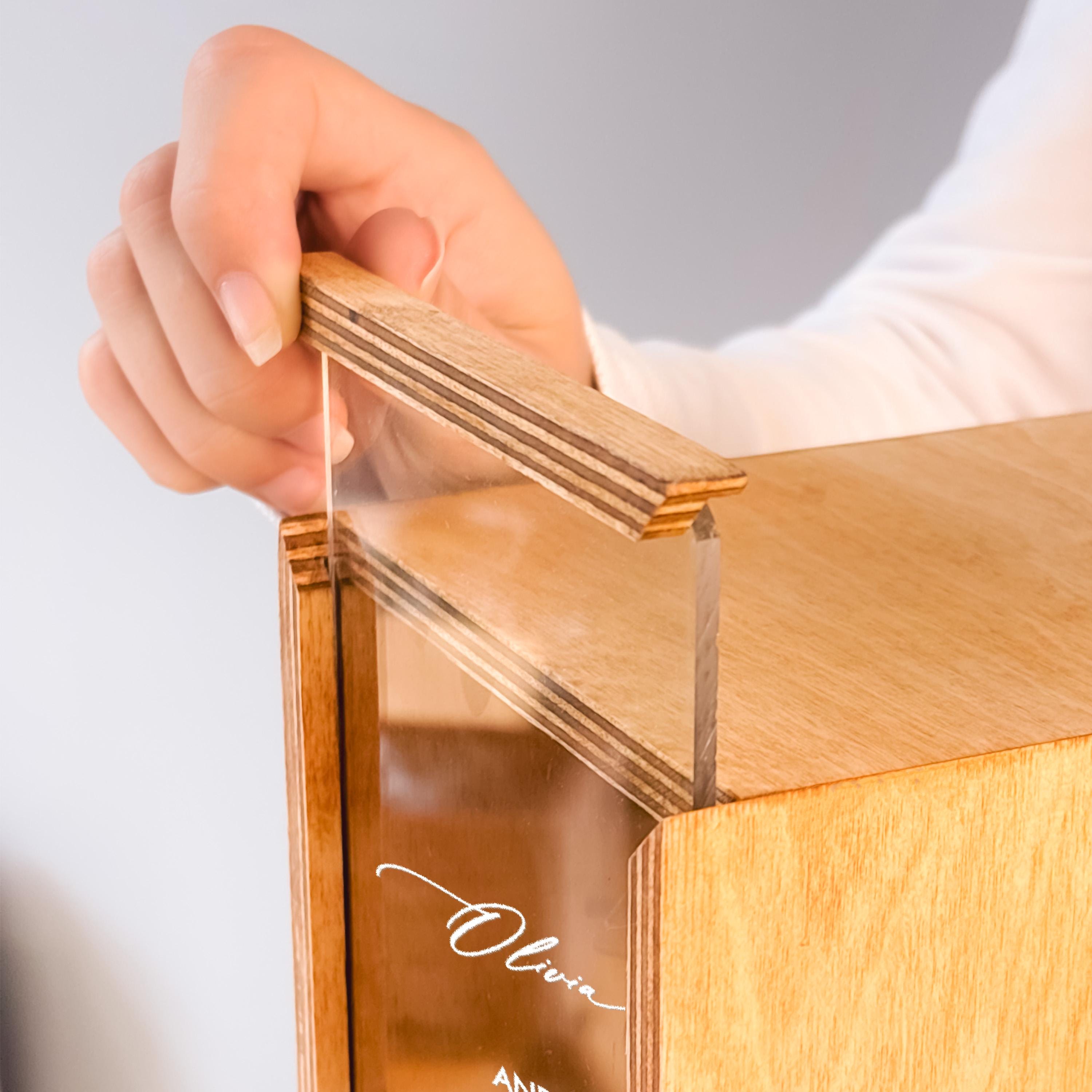A person's hand is holding a wooden handle with a clear glass panel, which appears to be a wooden box or container.
